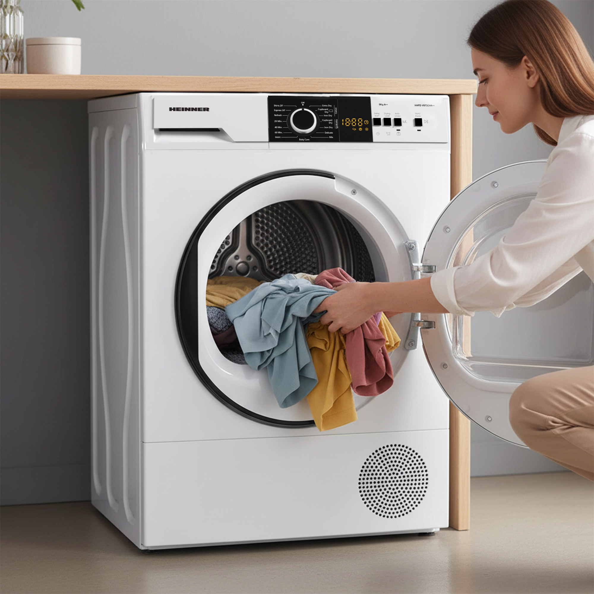 Eine Frau lädt Wäsche in einen weißen Trockner. Bunte Kleidung ist sichtbar.