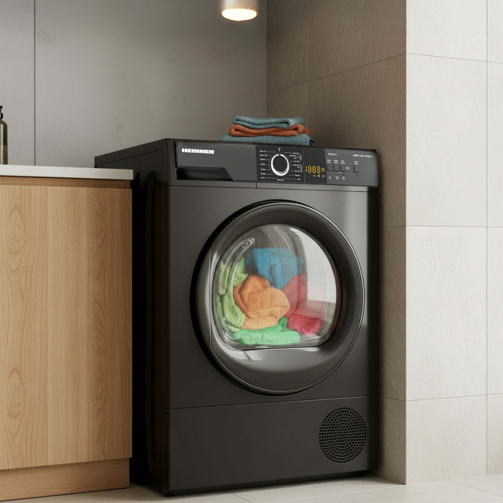Black dryer with colorful clothes inside the drum, next to a wooden cabinet.