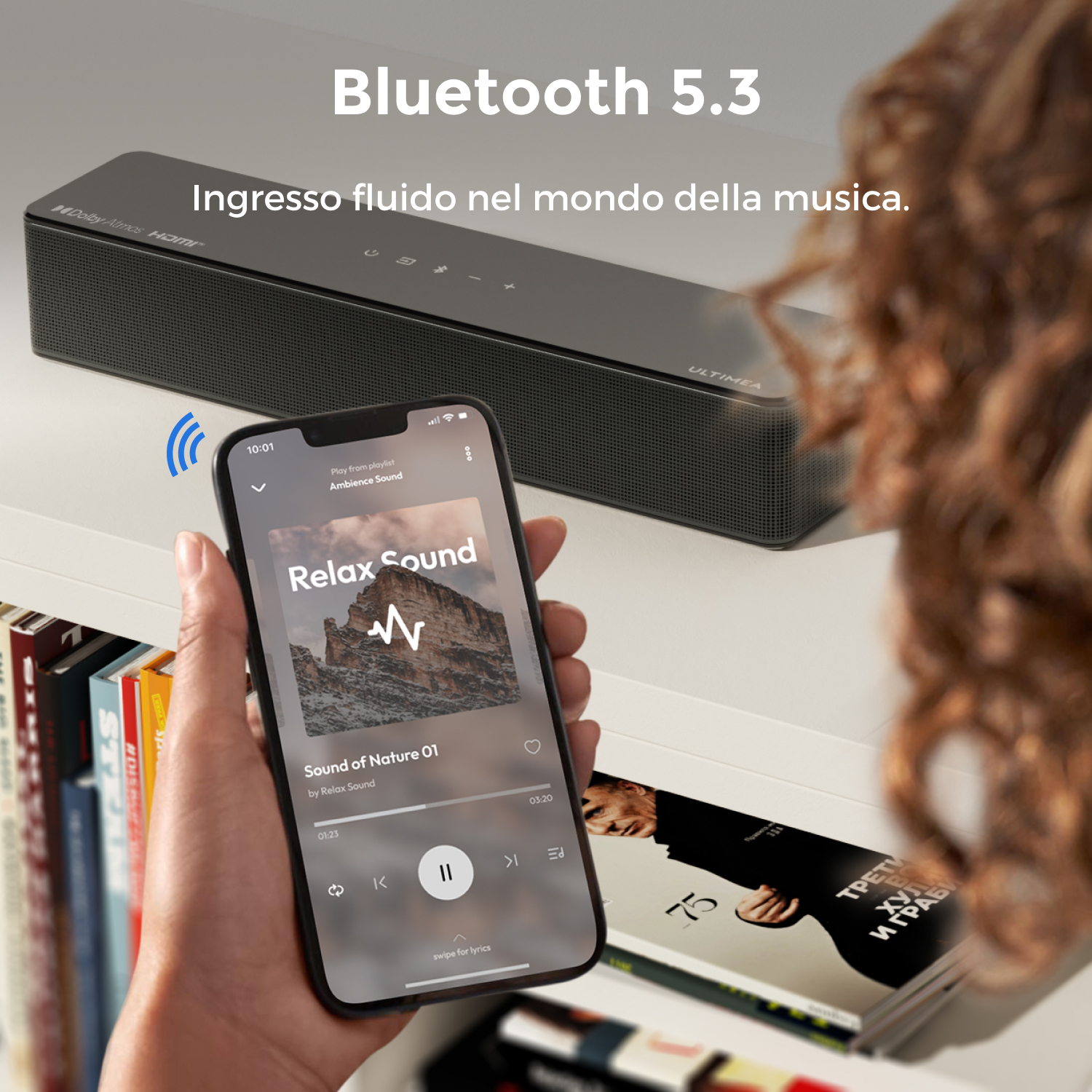 Una persona tiene uno smartphone con un'app musicale accanto a una soundbar nera.