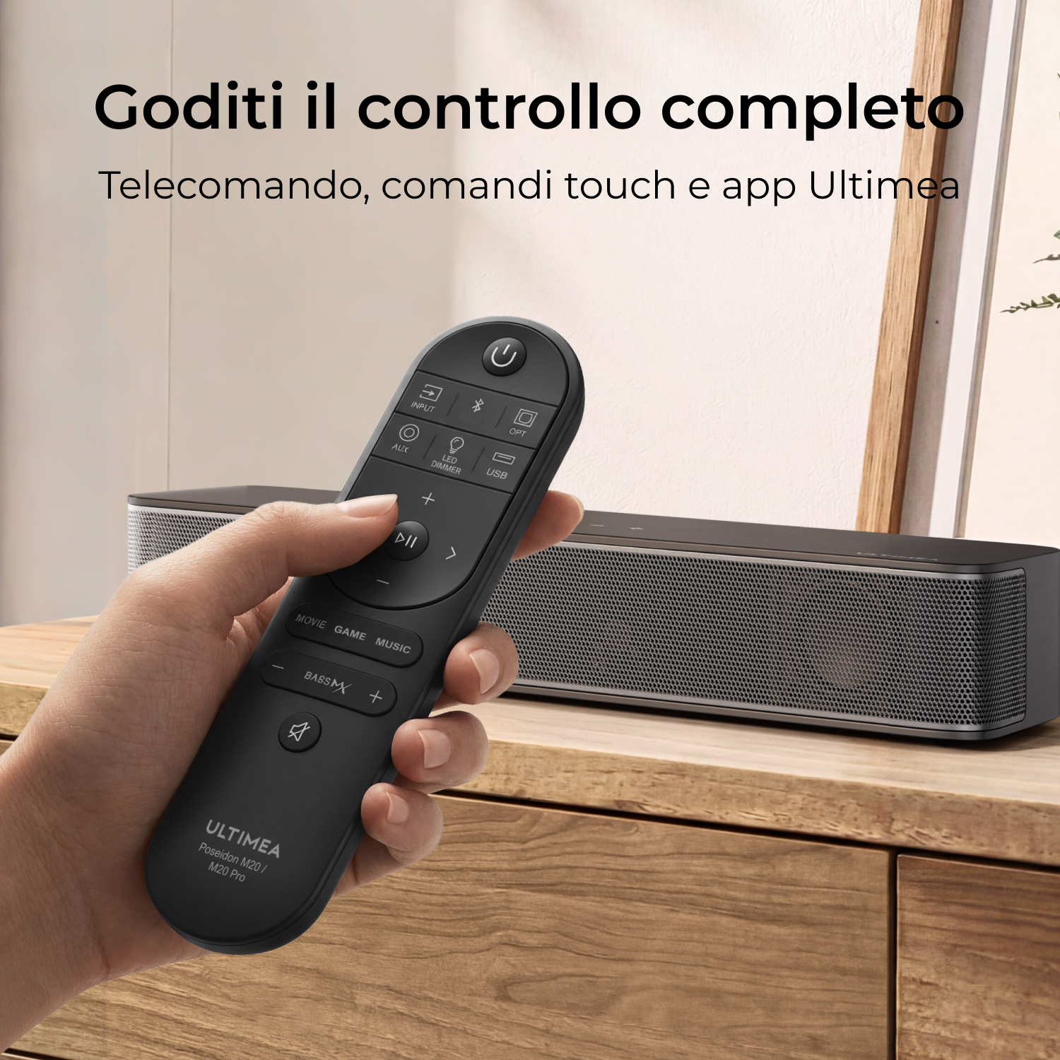 Mano tiene telecomando nero per soundbar Ultimea davanti a mobile in legno.