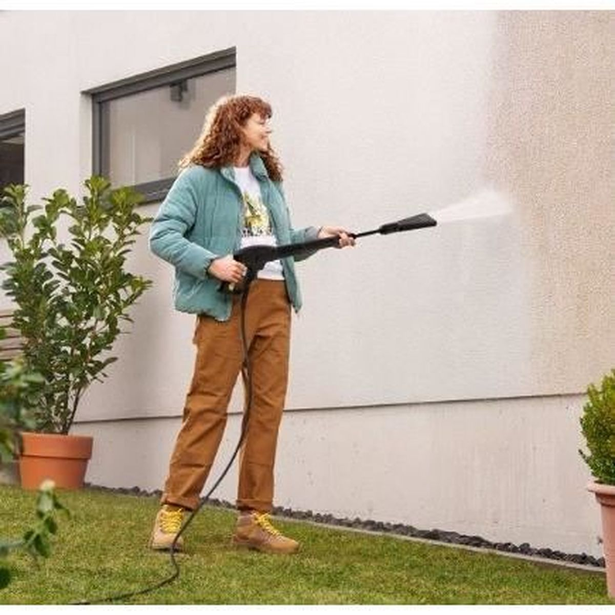 Donna pulisce muro di casa con idropulitrice in giardino.