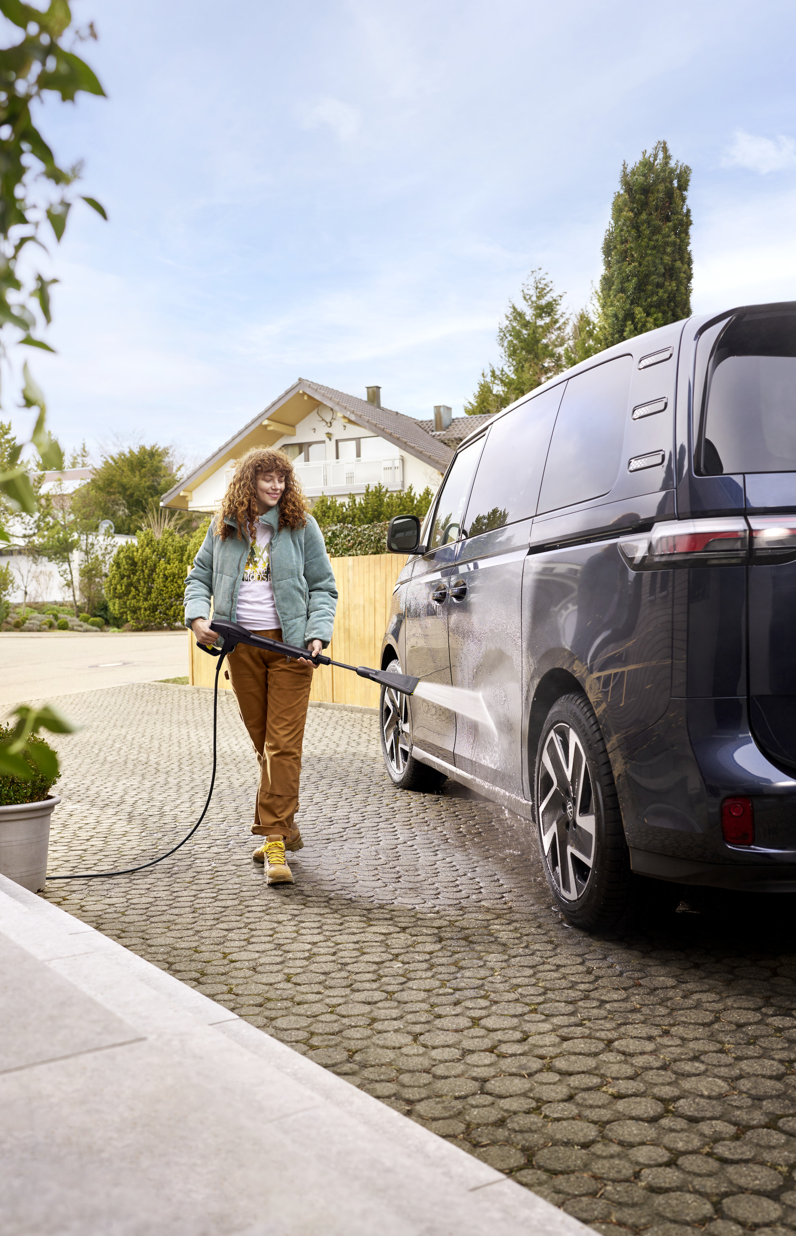 Donna lava auto con idropulitrice su vialetto pavimentato con bel tempo.