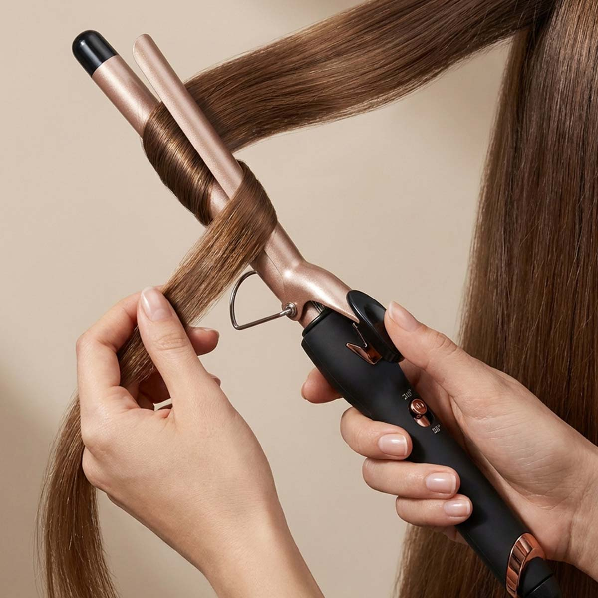 Eine Person lockt braunes Haar mit einem Lockenstab mit roséfarbenem Metall.