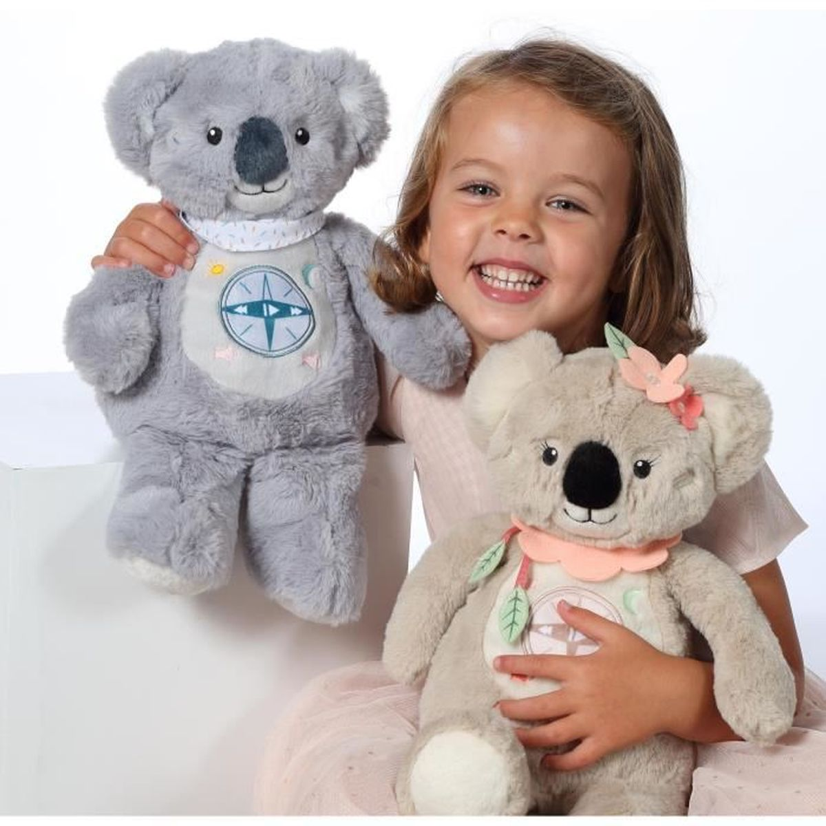 Ein kleines Mädchen lacht und hält zwei Koala-Stofftiere.