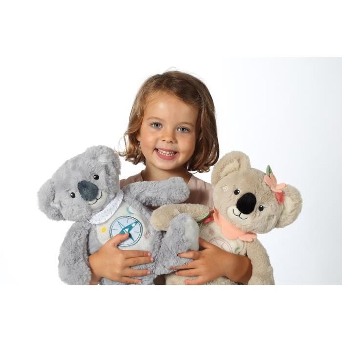 Ein kleines Mädchen hält zwei Koala-Stofftiere, eines grau und eines beige.