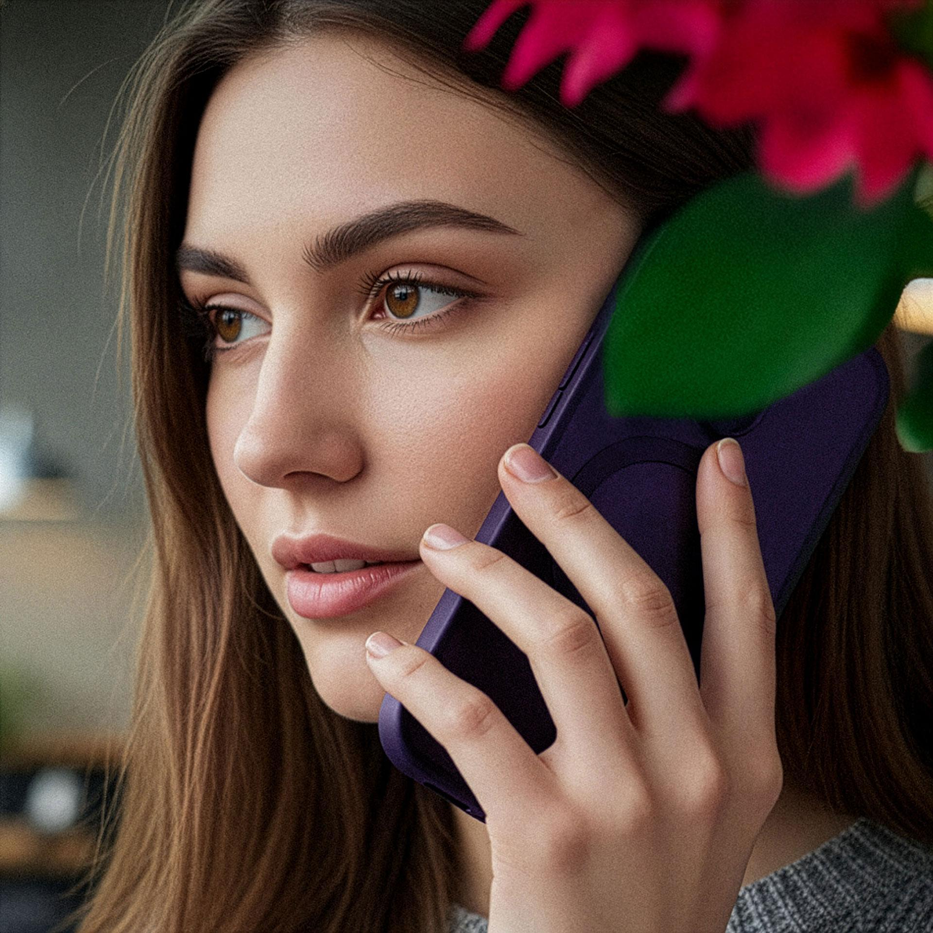 Donna con capelli castani parla al telefono viola, con fiori rosa davanti.