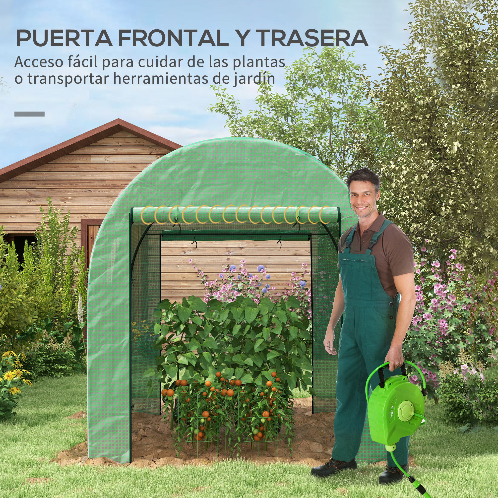 Hombre con overol verde sostiene manguera de jardín frente a invernadero.