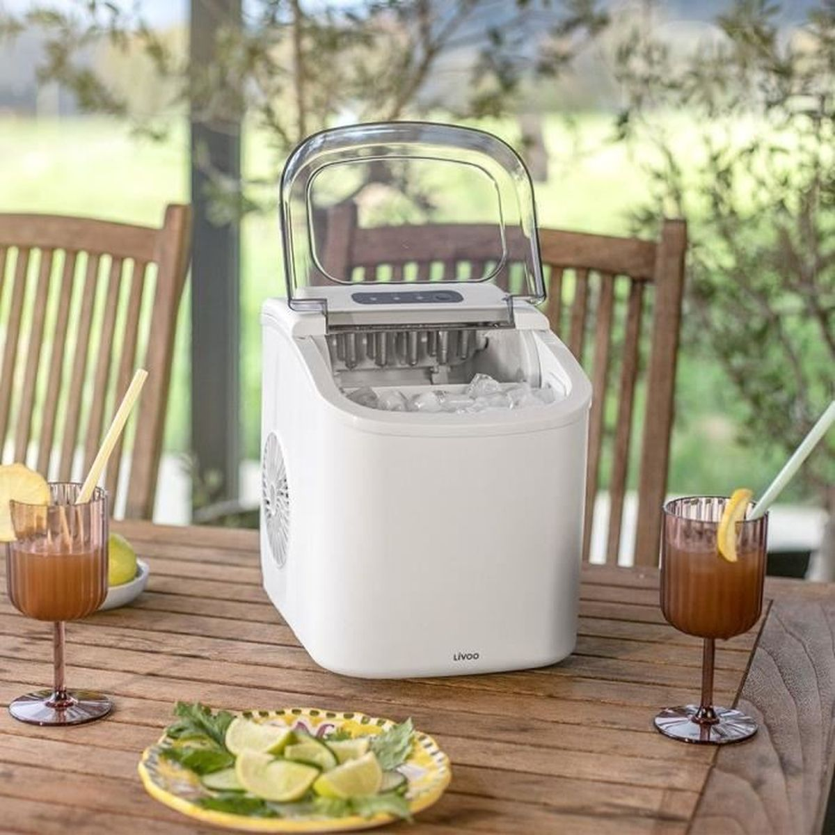 Eine weiße Eismaschine auf einem Holztisch mit Getränken und Limettenscheiben.