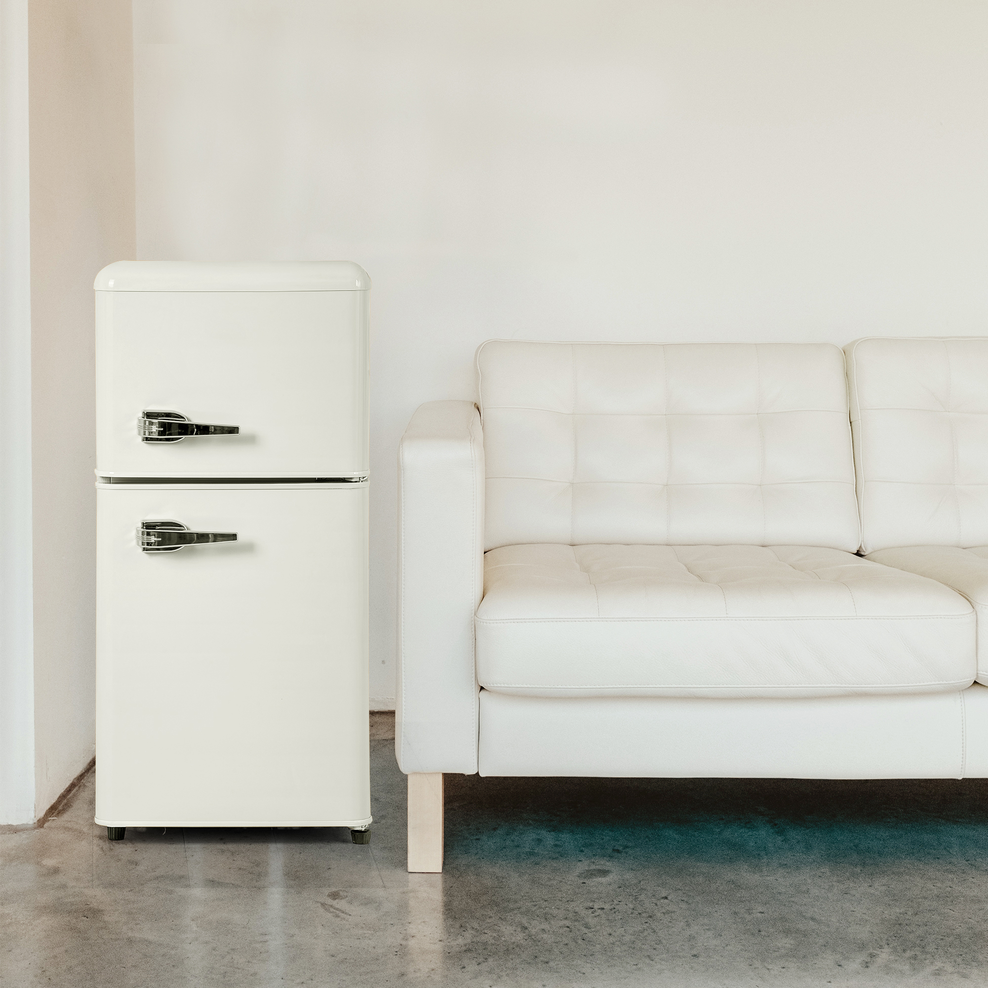 Ein cremefarbener Kühlschrank neben einem weißen Ledersofa auf Betonboden.