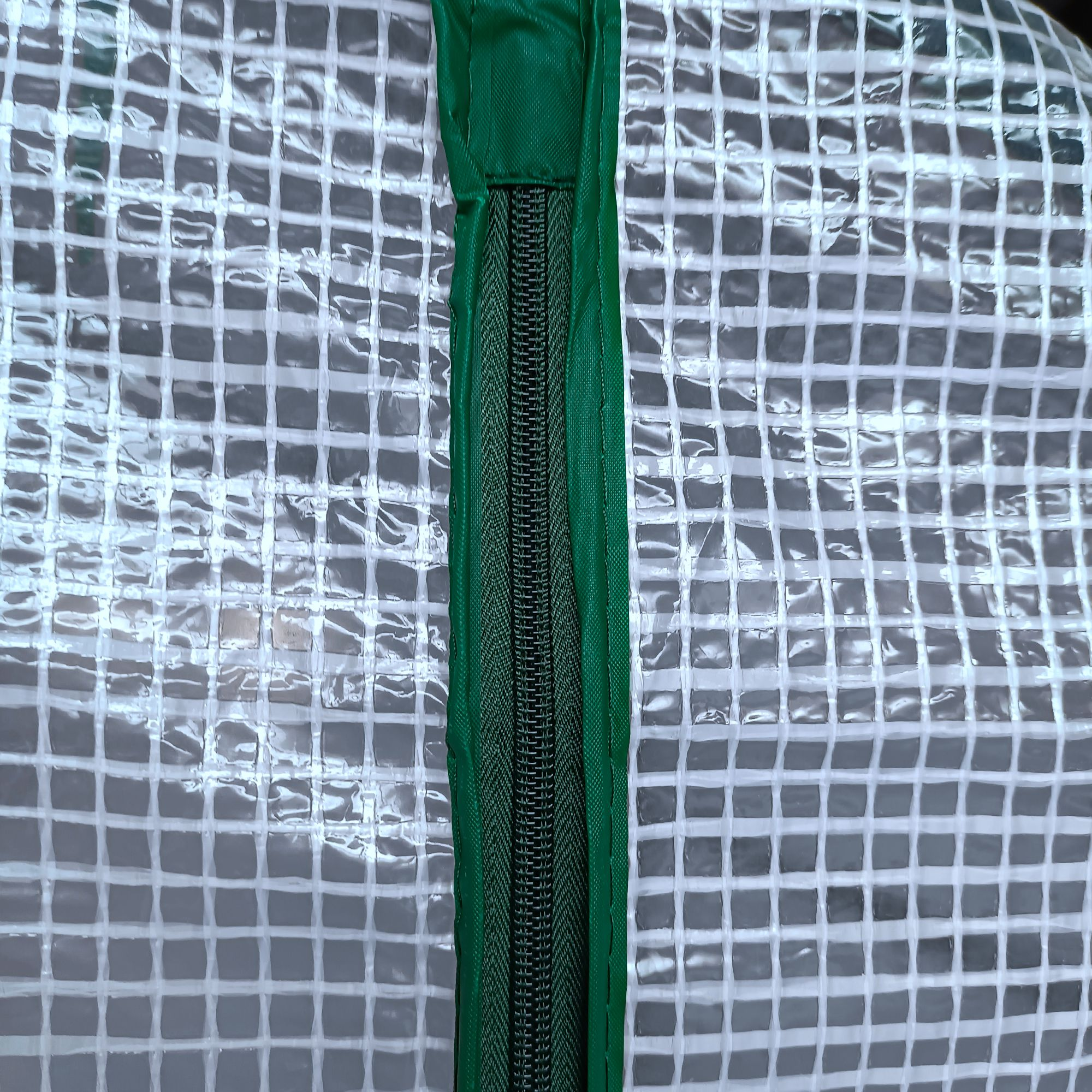 Primer plano de una cremallera verde en una lona de plástico transparente y cuadriculada.
