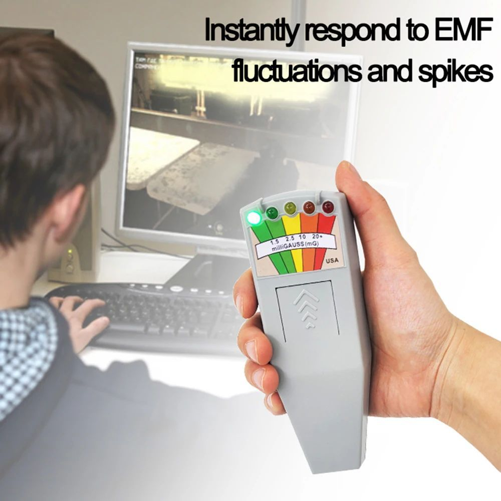 Eine Hand hält ein graues EMF-Messgerät vor einem Computer.