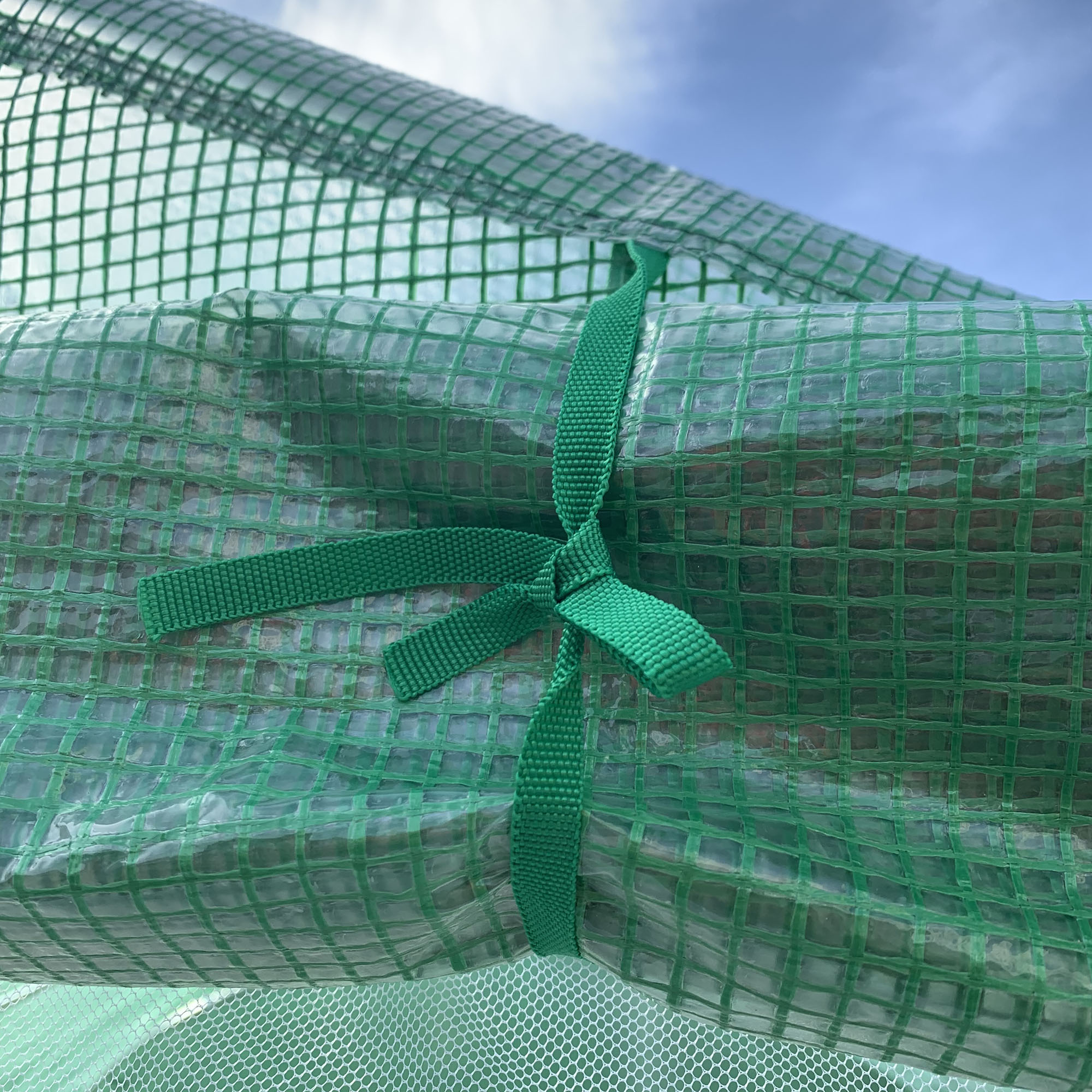 Tejido de malla verde enrollado y atado con una correa, contra un cielo azul.