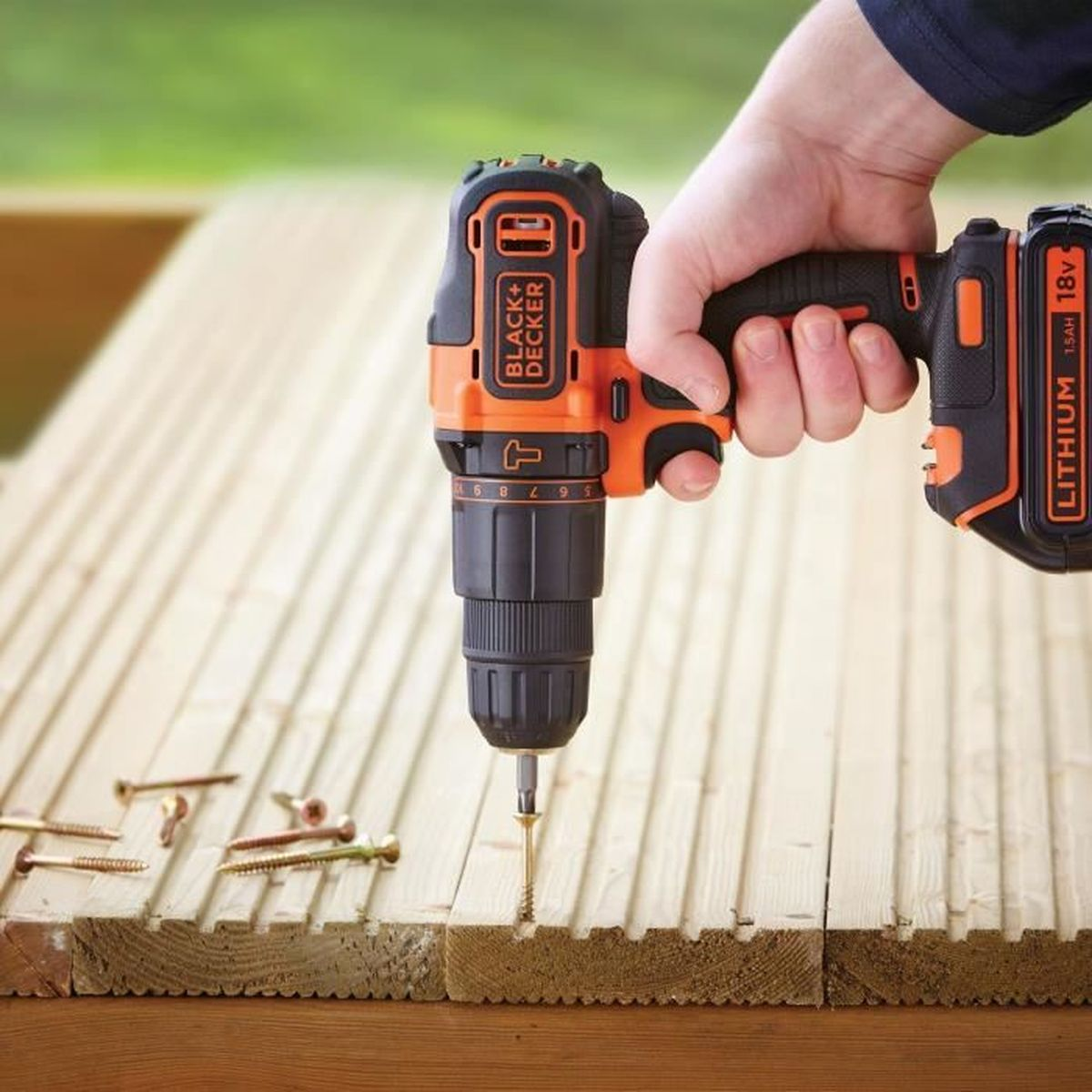 Hand bohrt Schraube in Holzbrett. Werkzeug ist orange und schwarz.