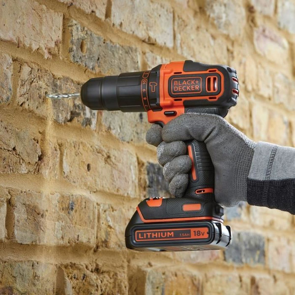 Ein Handschuh hält einen Bohrer, der in eine Ziegelwand bohrt.