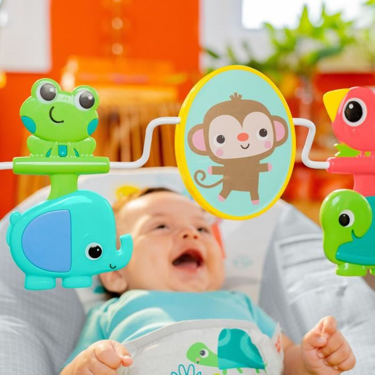 Ein Baby lacht unter Spielzeug mit Tieren wie einem Elefanten und Affen.