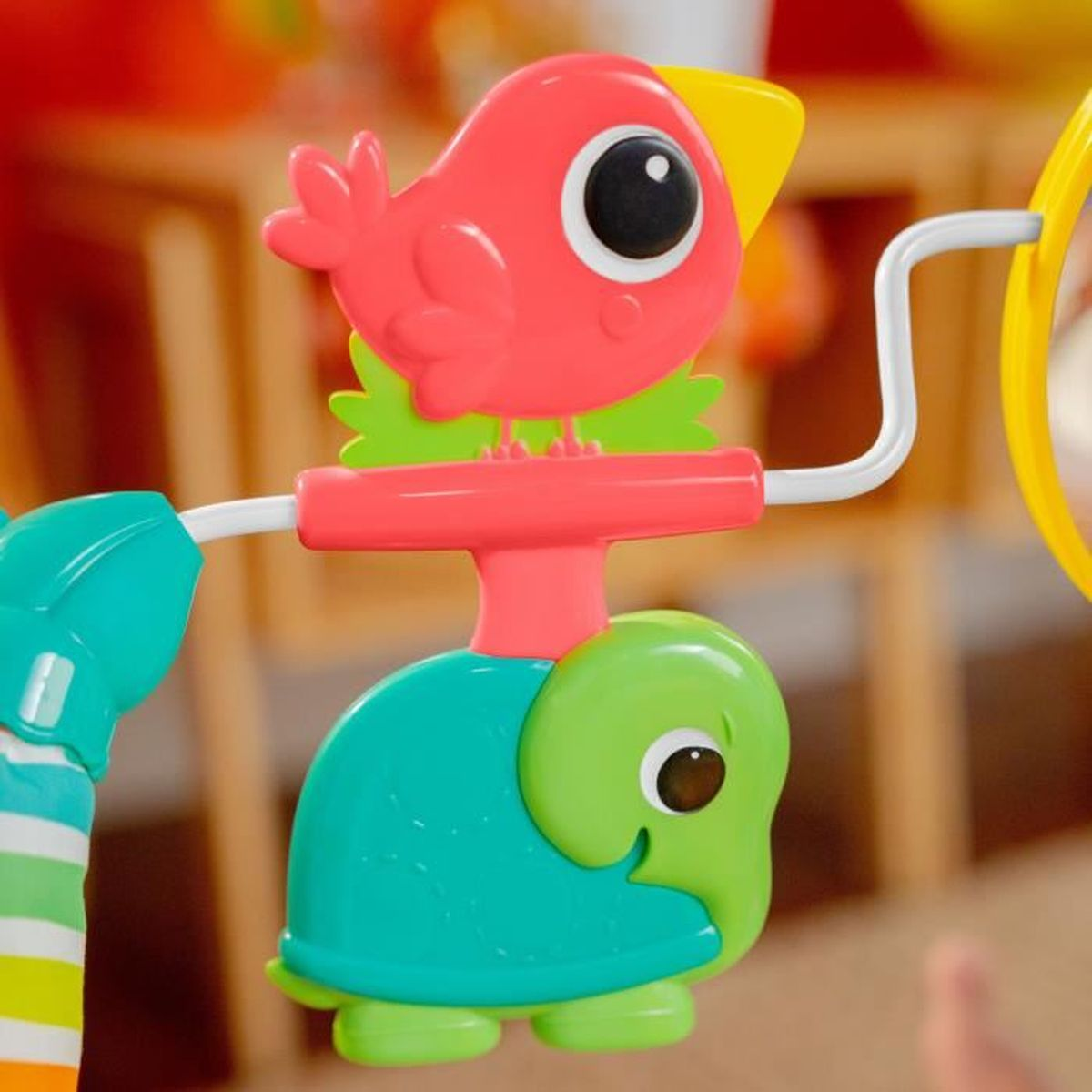 Ein bunter Spielzeug-Vogel und eine Schildkröte hängen an einem Spielbogen.