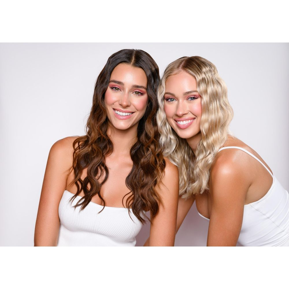 Zwei Frauen mit langen, welligen Haaren und rosa Lidschatten, die lächeln.