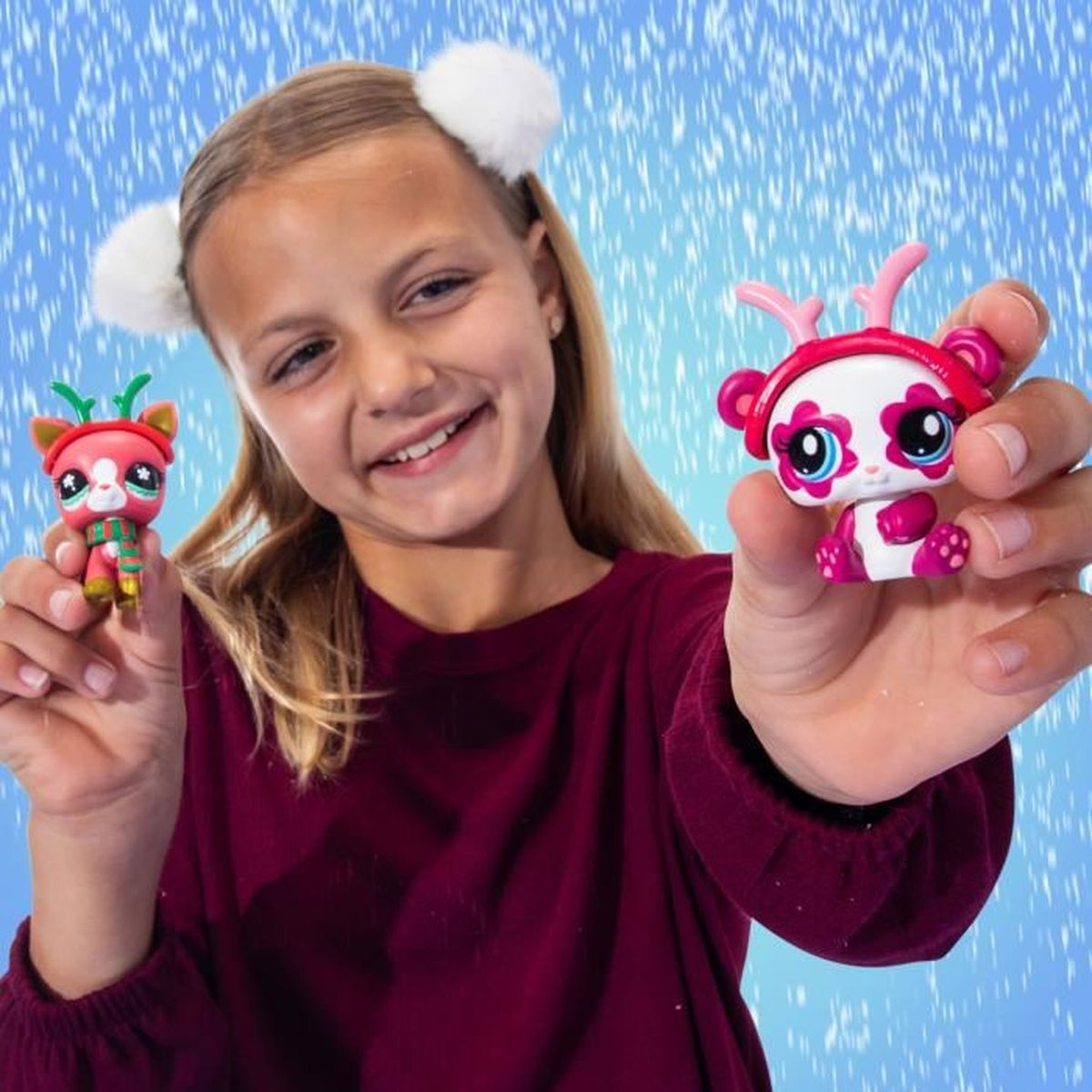 Ein Mädchen mit weißen Pompons am Kopf hält zwei Spielzeugtiere, eines rot, das andere weiß und pink.