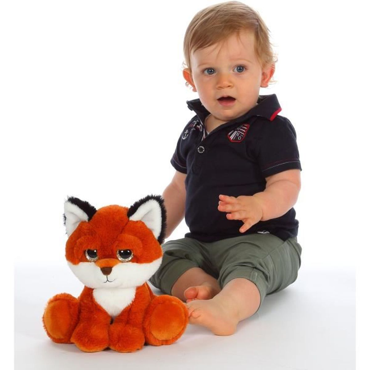 Un bébé assis à côté d'un renard en peluche sur fond blanc.