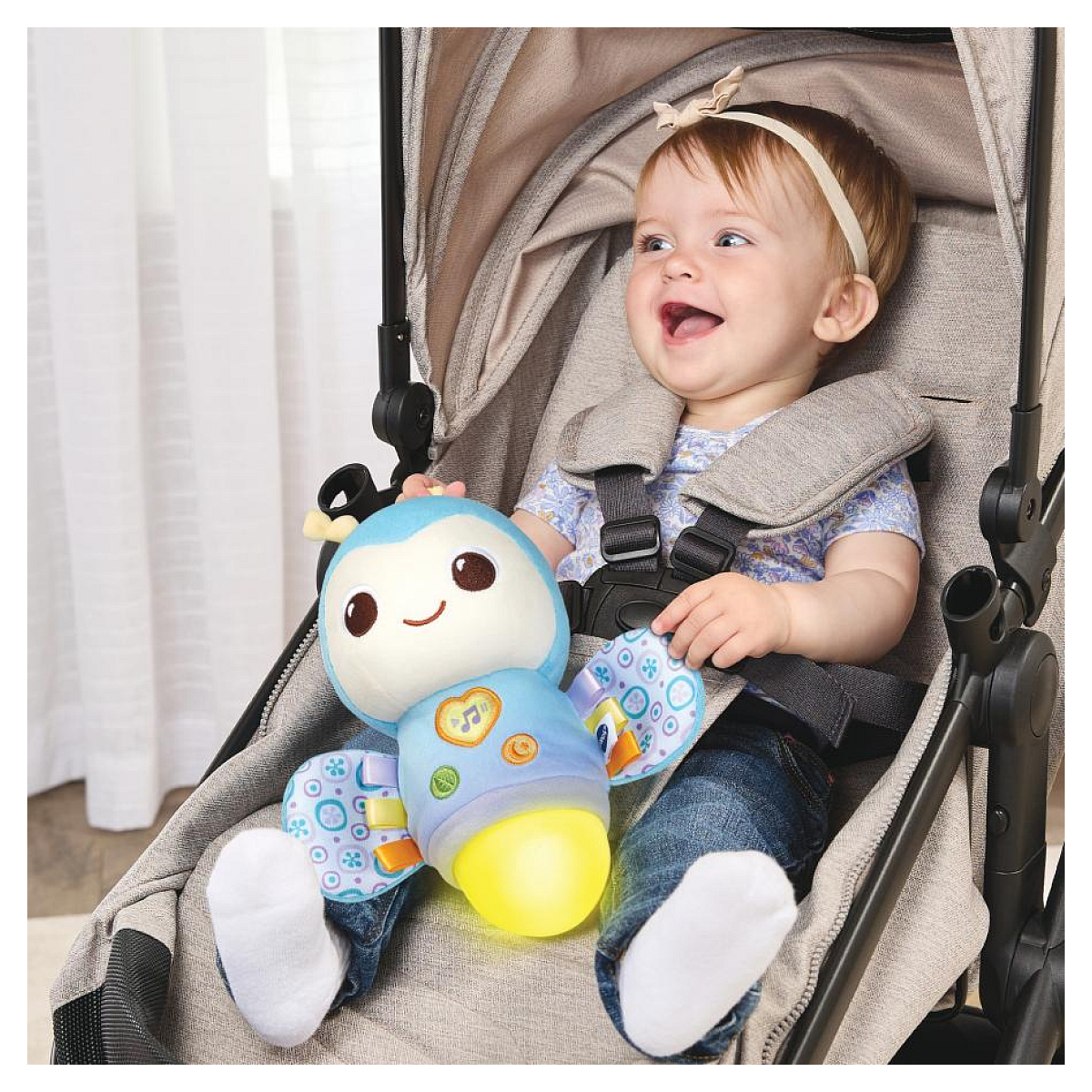 Ein Baby sitzt in einem Kinderwagen und hält ein blaues Spielzeug. Es lacht.