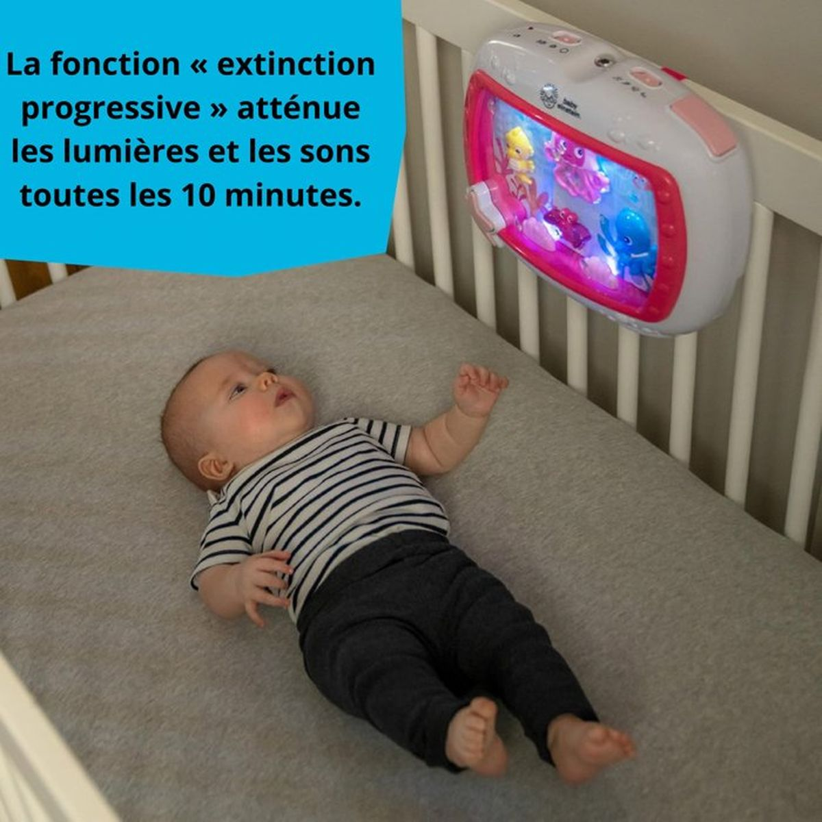 Ein Baby liegt im Bett und schaut auf ein Nachtlicht mit Figuren, das Lichter und Töne abgibt.
