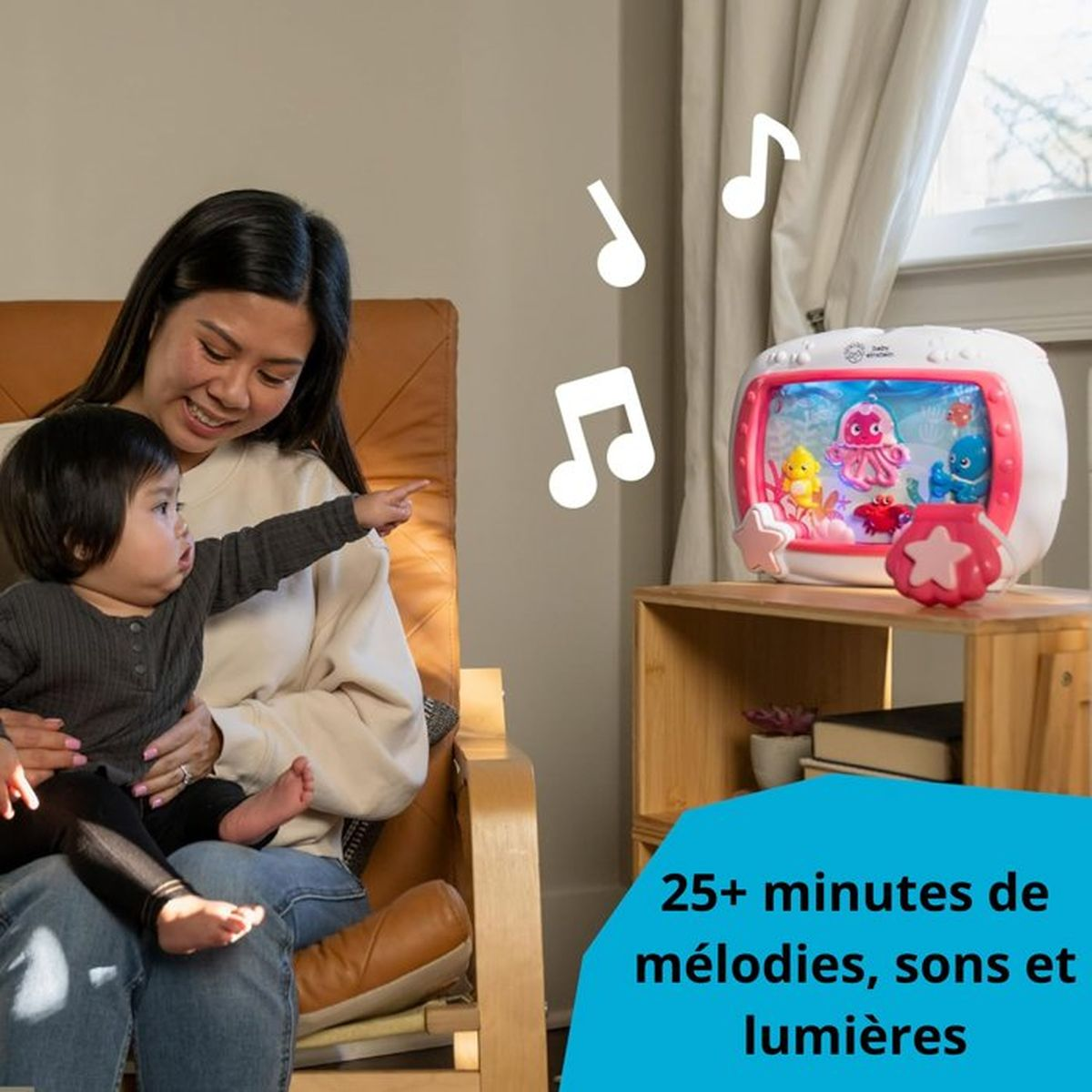 Mutter hält Baby, das auf Spielzeug mit Meeresmotiven zeigt. Musiknoten schweben.