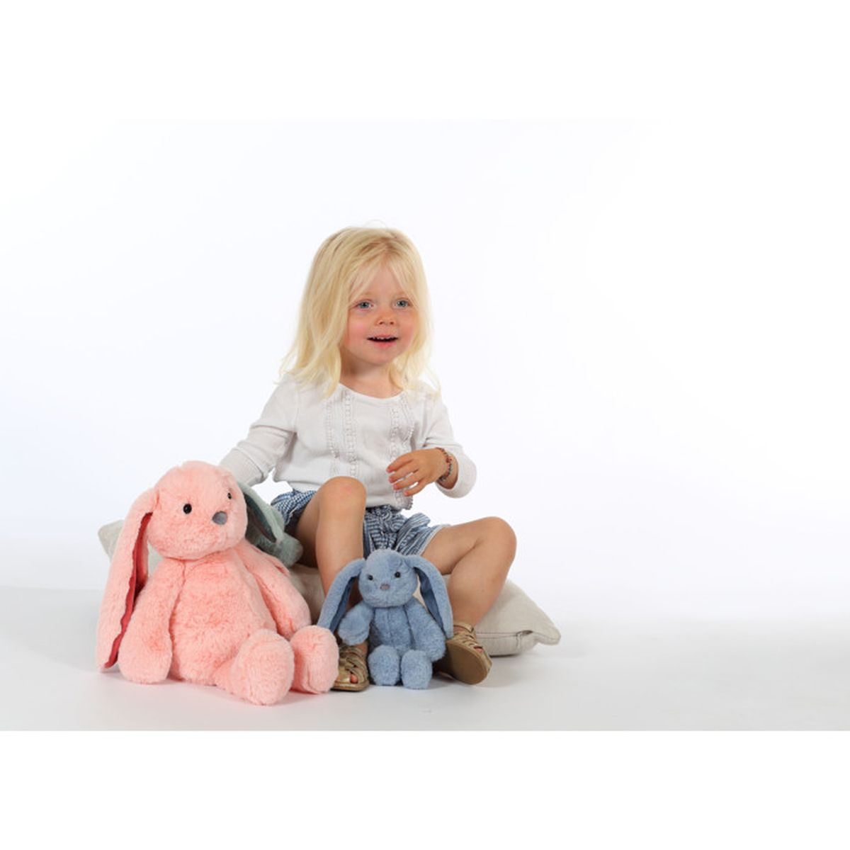 Ein kleines Mädchen sitzt mit zwei Stoffhasen.