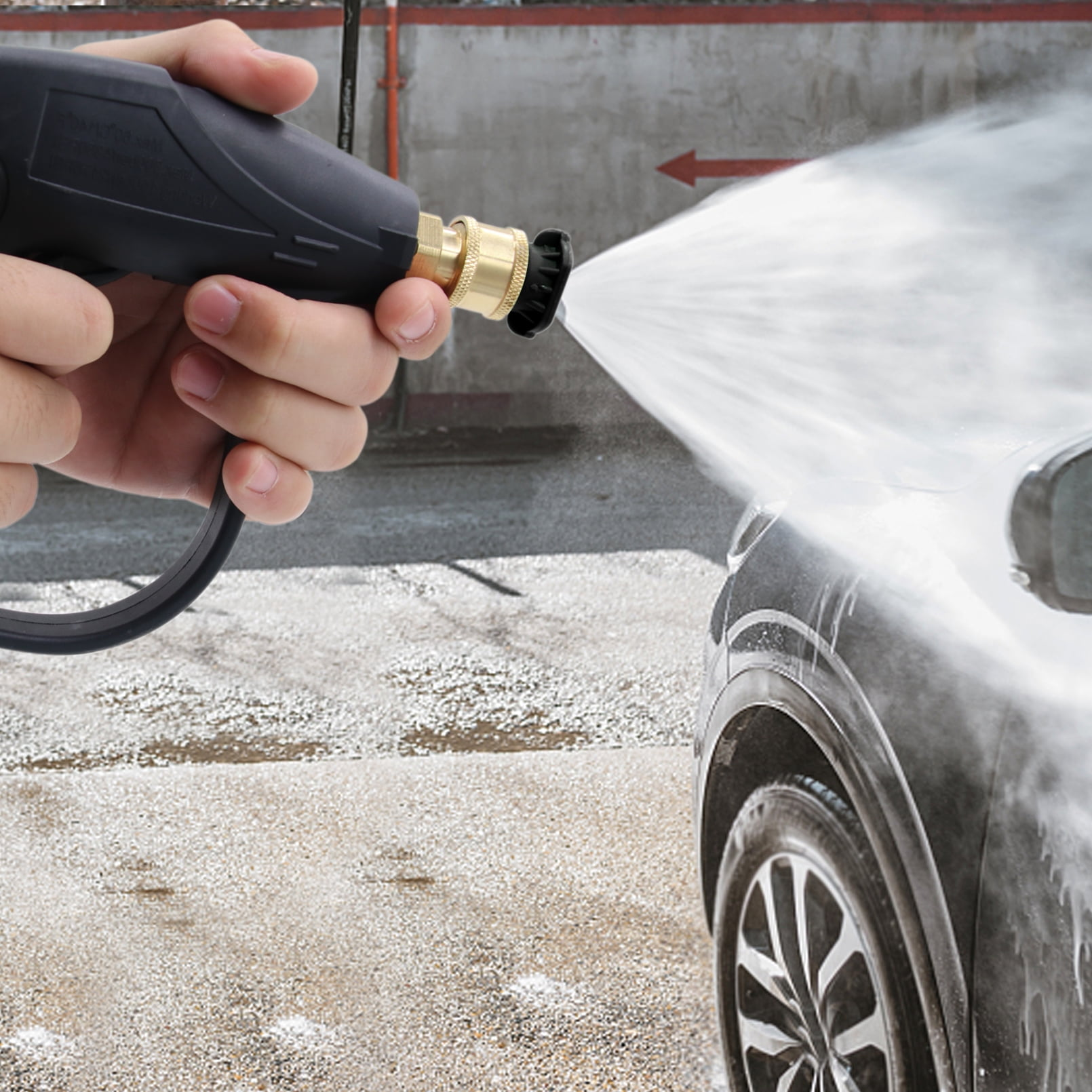 Hand hält Hochdruckreiniger, der Wasser auf schwarzes Autoteil sprüht.