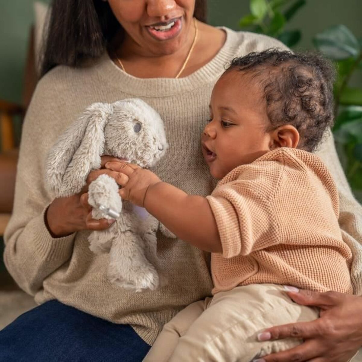 Eine Frau hält ein Baby und ein Plüschhasen. Das Baby greift nach dem Hasen.