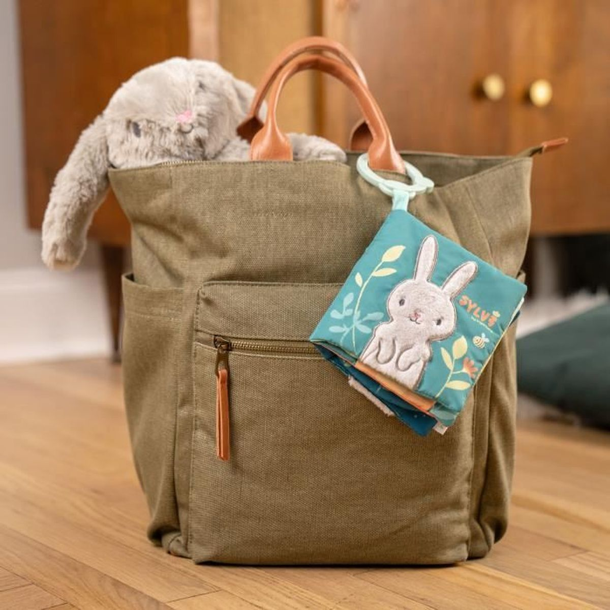 Ein Stoffhase und ein Buch mit Hasenmotiv stecken in einer olivgrünen Tasche.