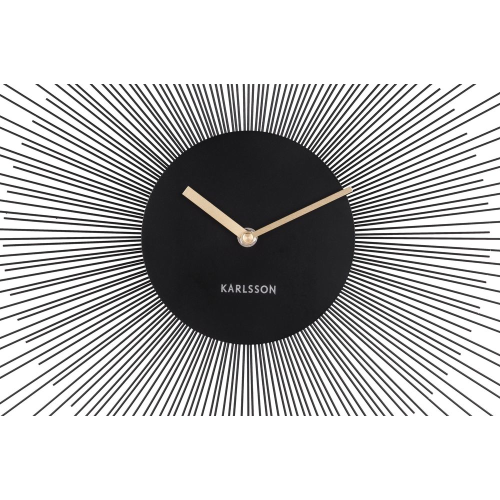 Une horloge murale noire avec des aiguilles dorées et un design en rayons de soleil.