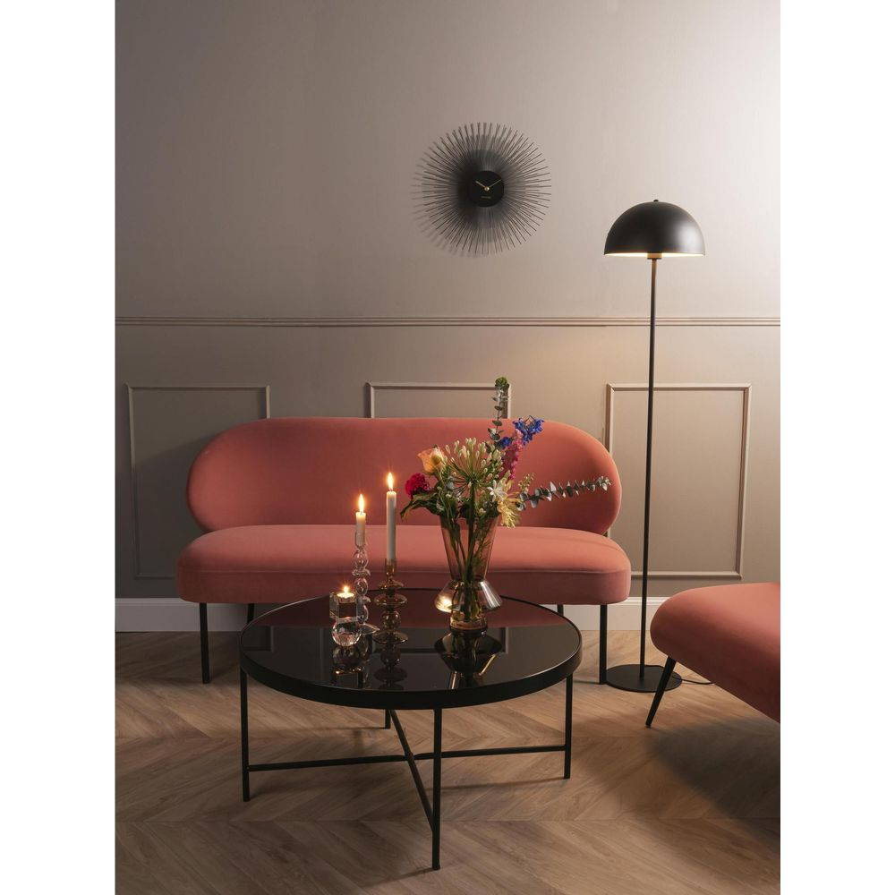 Un canapé pêche, table basse ronde avec bougies et fleurs, lampadaire et horloge murale.