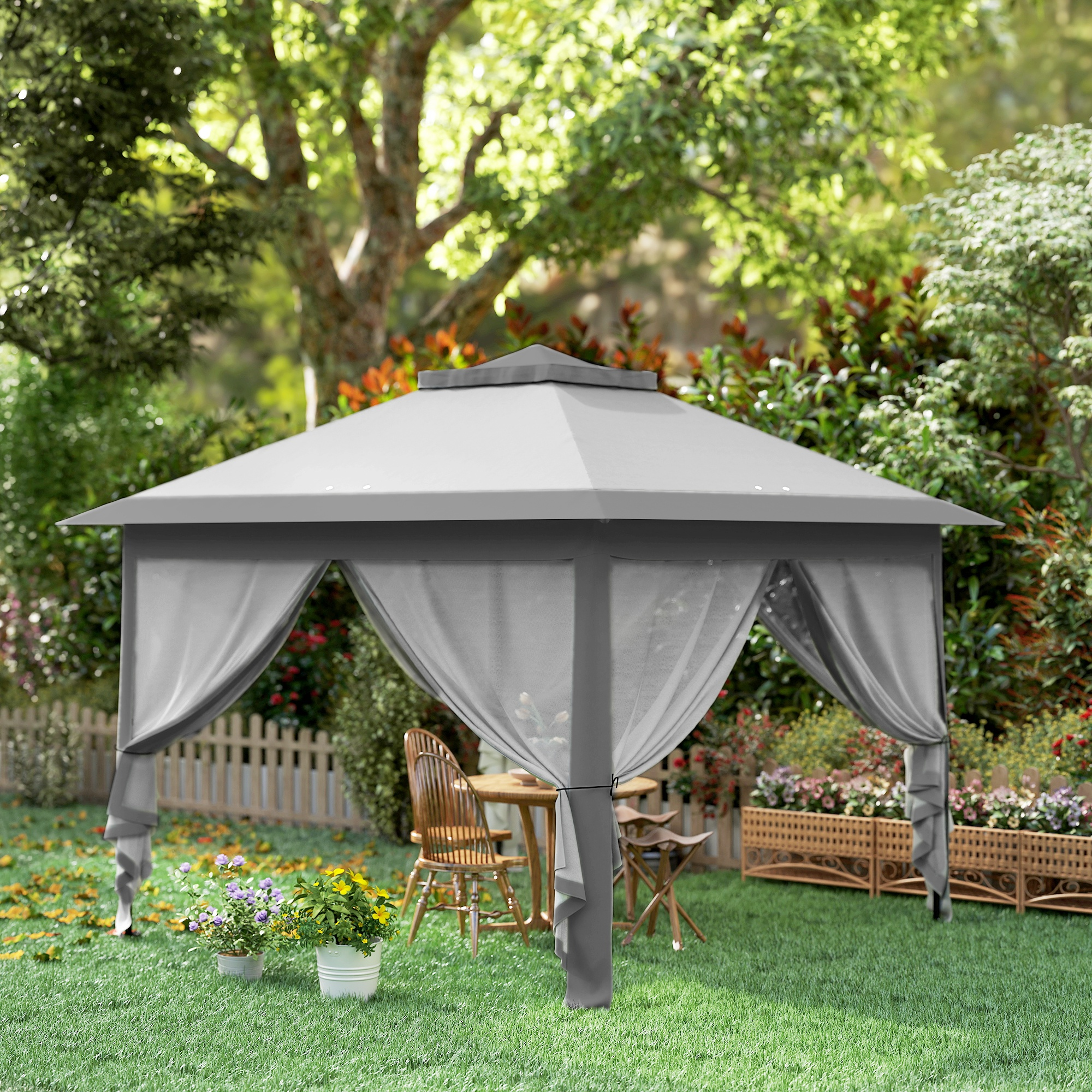 Un gazebo grigio con tende si trova su un prato con fiori e mobili.