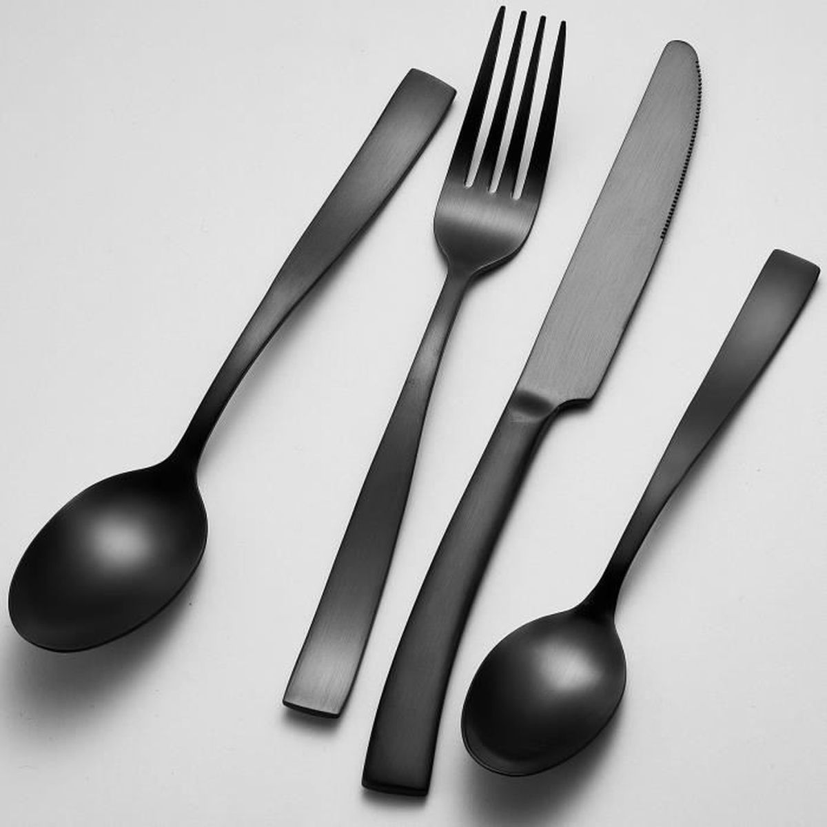 Vier schwarze Besteckteile: Löffel, Gabel, Messer, Löffel.
