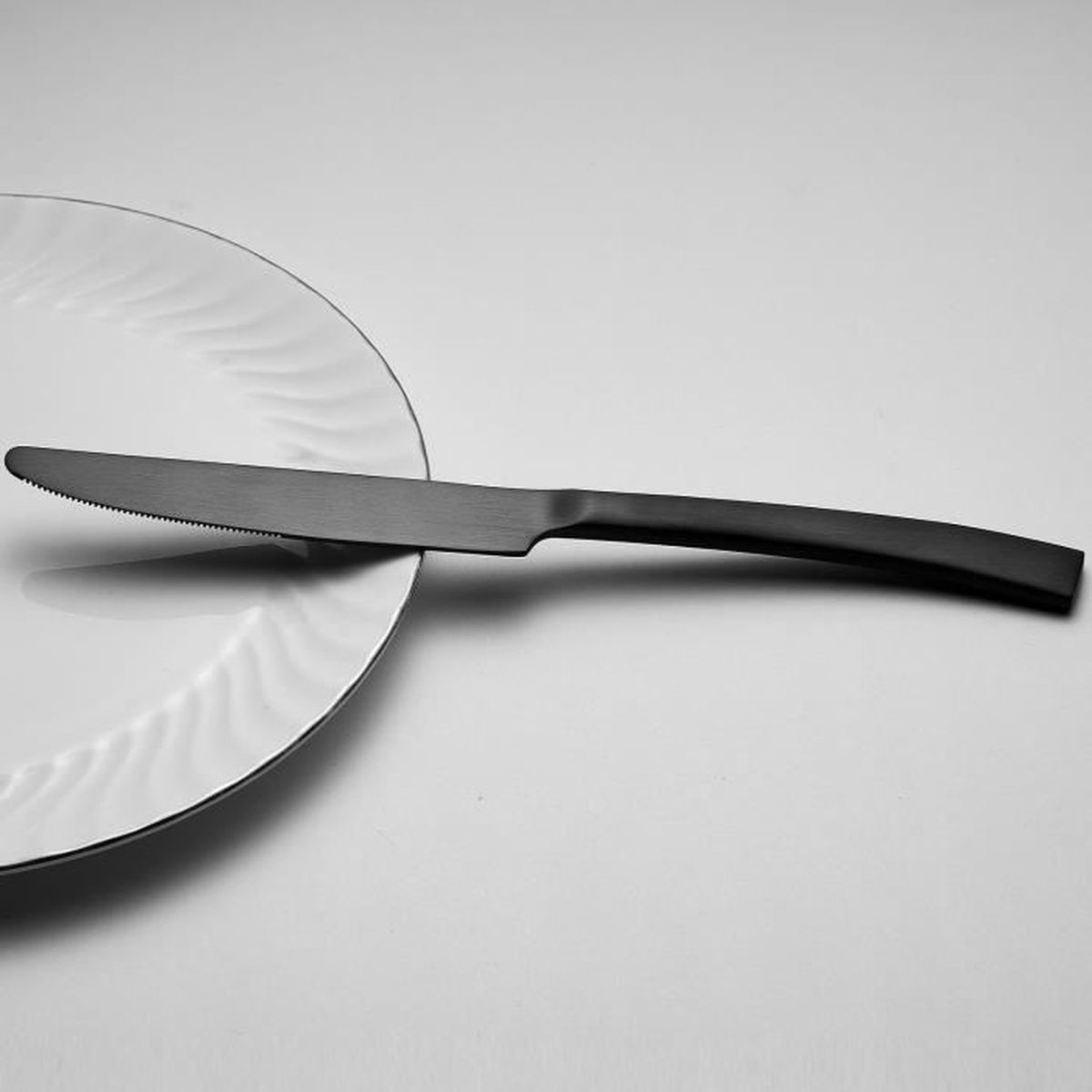 Ein schwarzes Messer liegt auf einem weißen Teller mit Rillen.