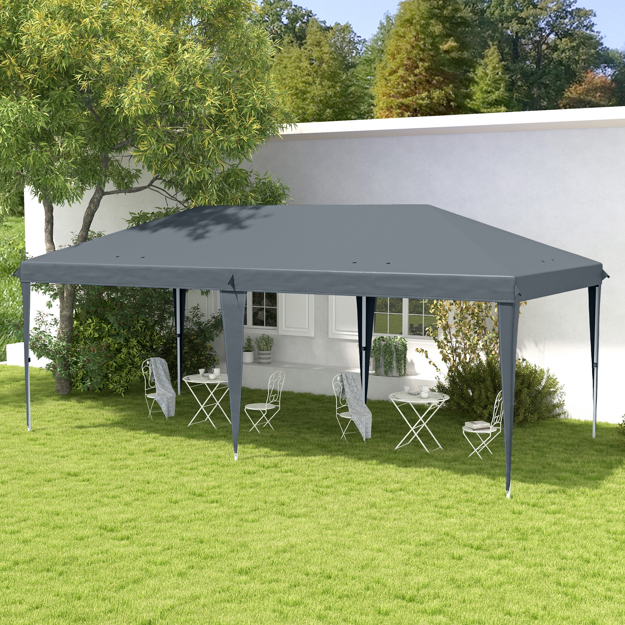 Una tenda a baldacchino grigia si trova in un giardino su erba verde con tavoli e sedie in metallo bianchi.