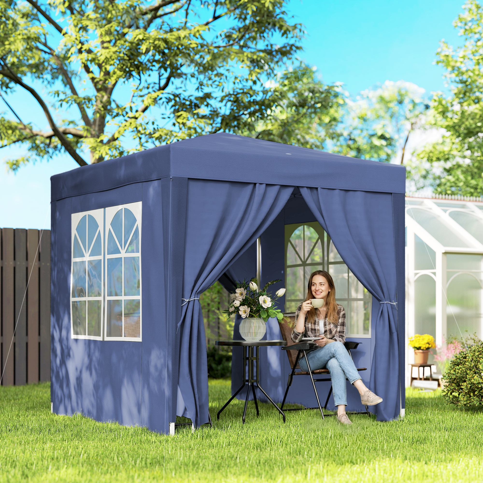 Una donna beve caffè sotto un gazebo blu in giardino, accanto a una serra.
