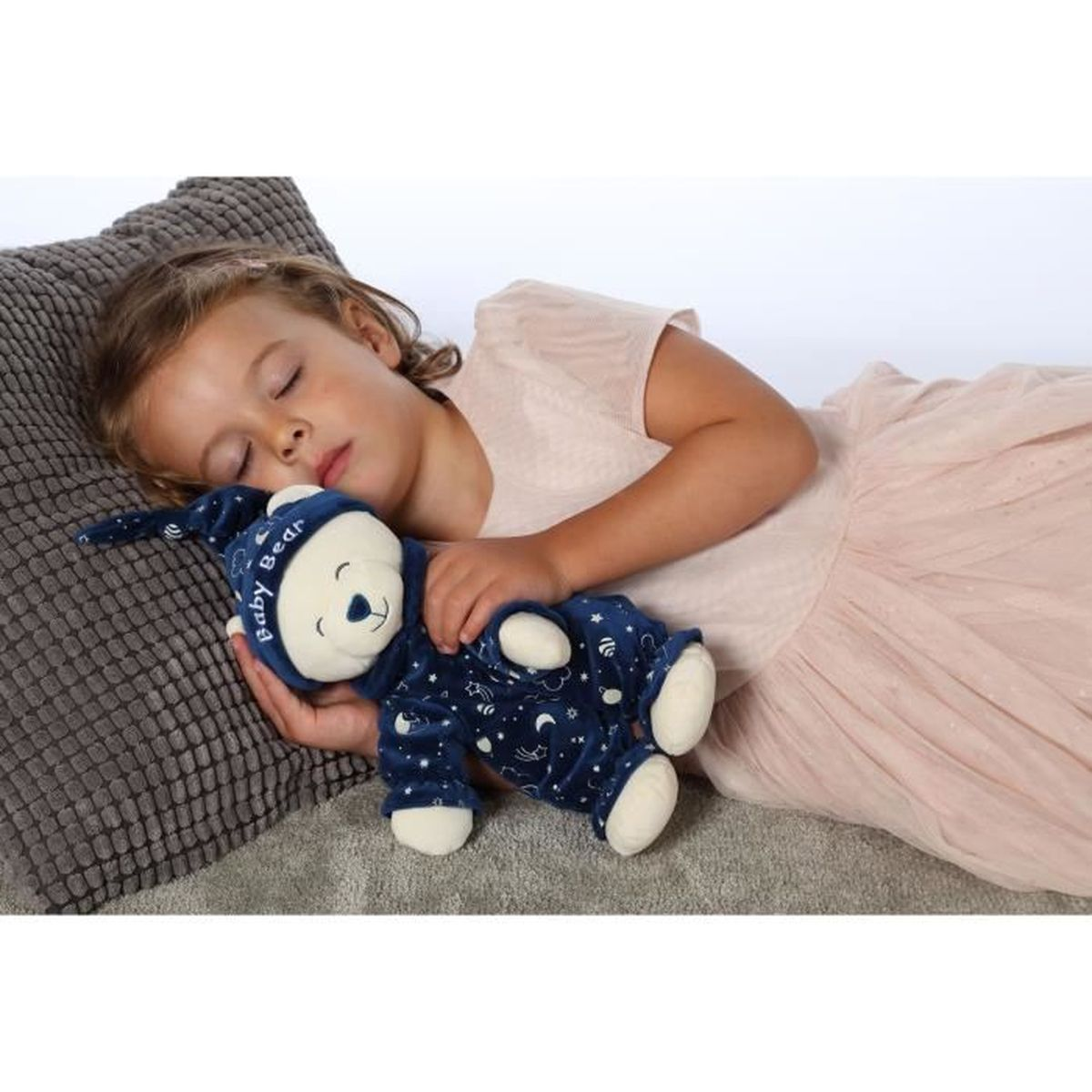 Une jeune fille dort avec un ours en peluche bleu sur un oreiller.