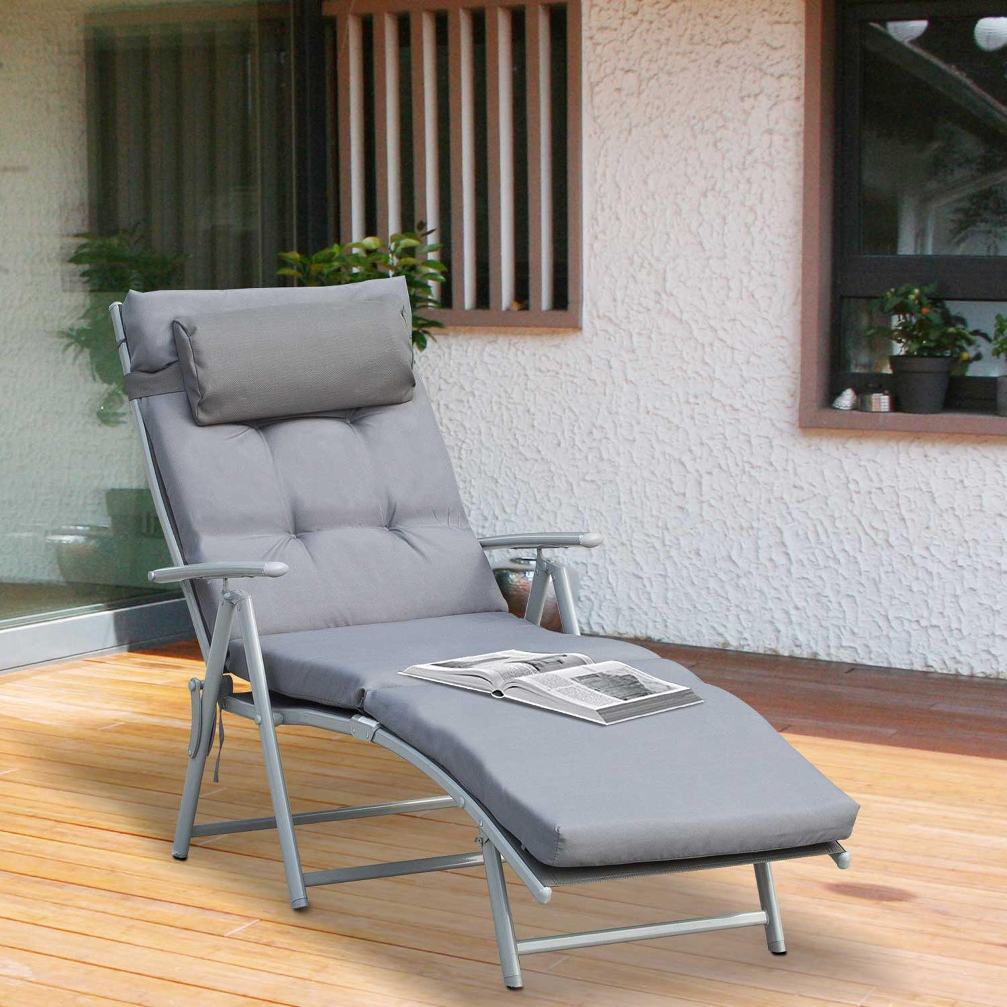Sdraio grigio con cuscino e libro su terrazza in legno.