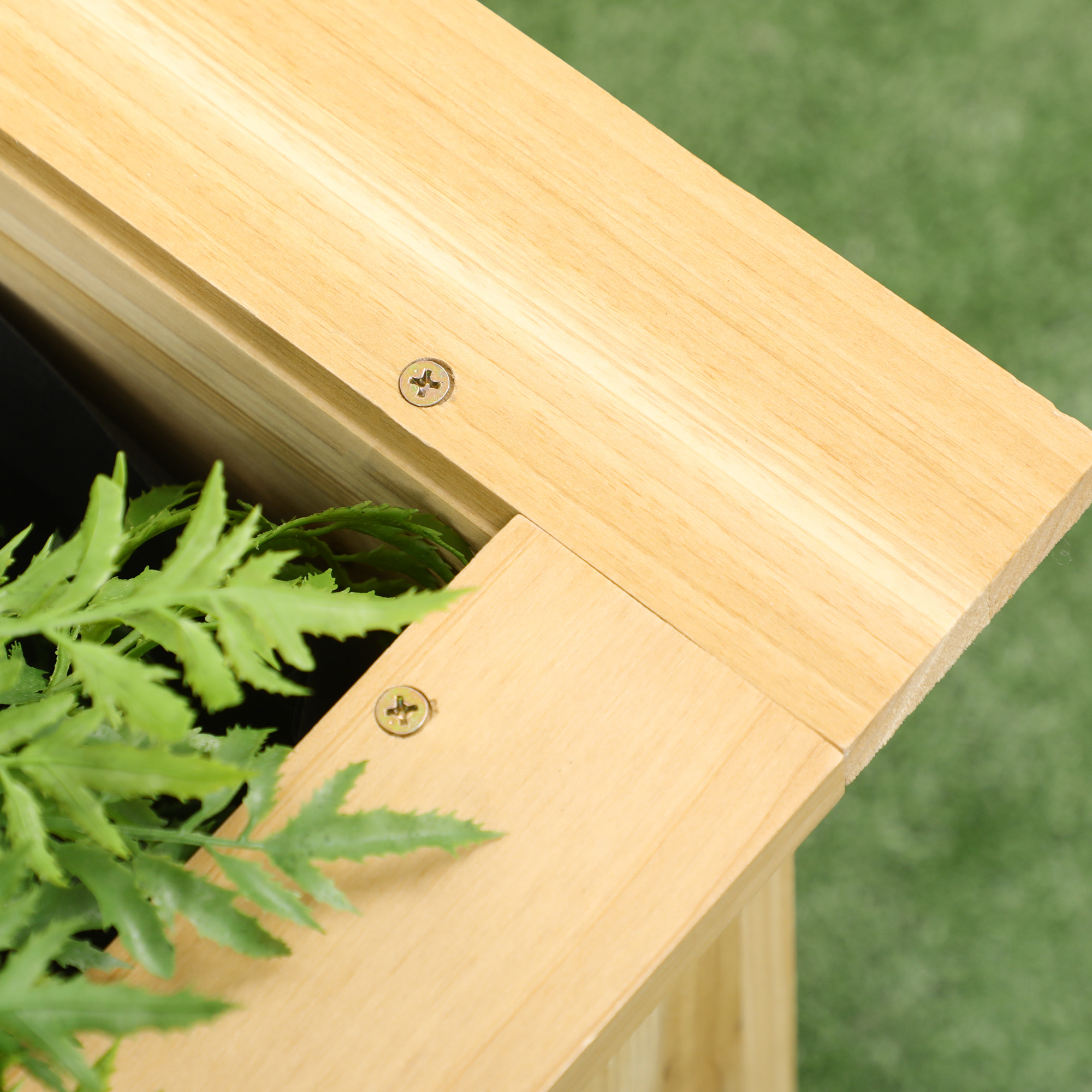 Macetero de madera con hojas verdes y tornillos, césped verde al fondo.