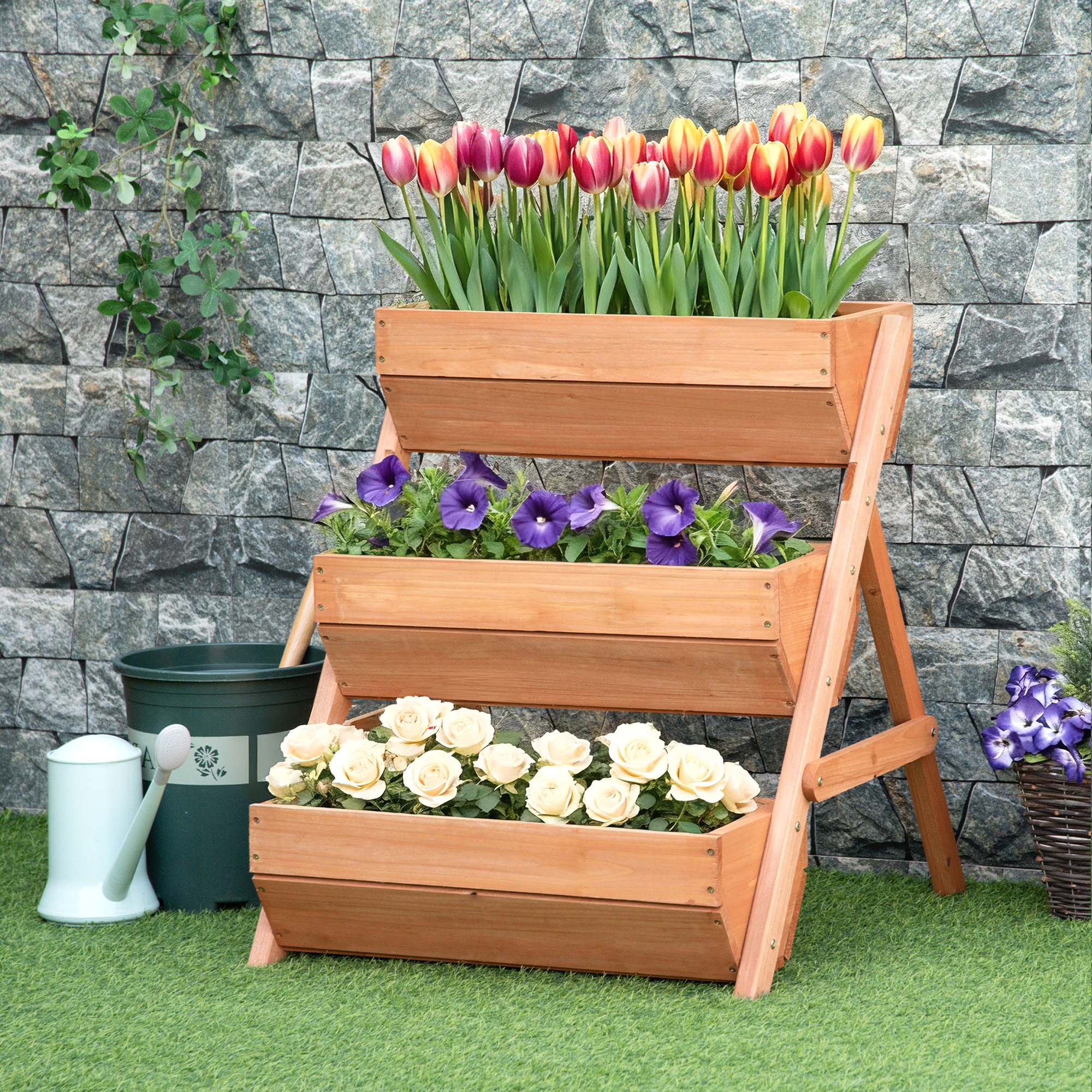 Una jardinera de madera de tres niveles con tulipanes, petunias y rosas contra un muro de piedra.