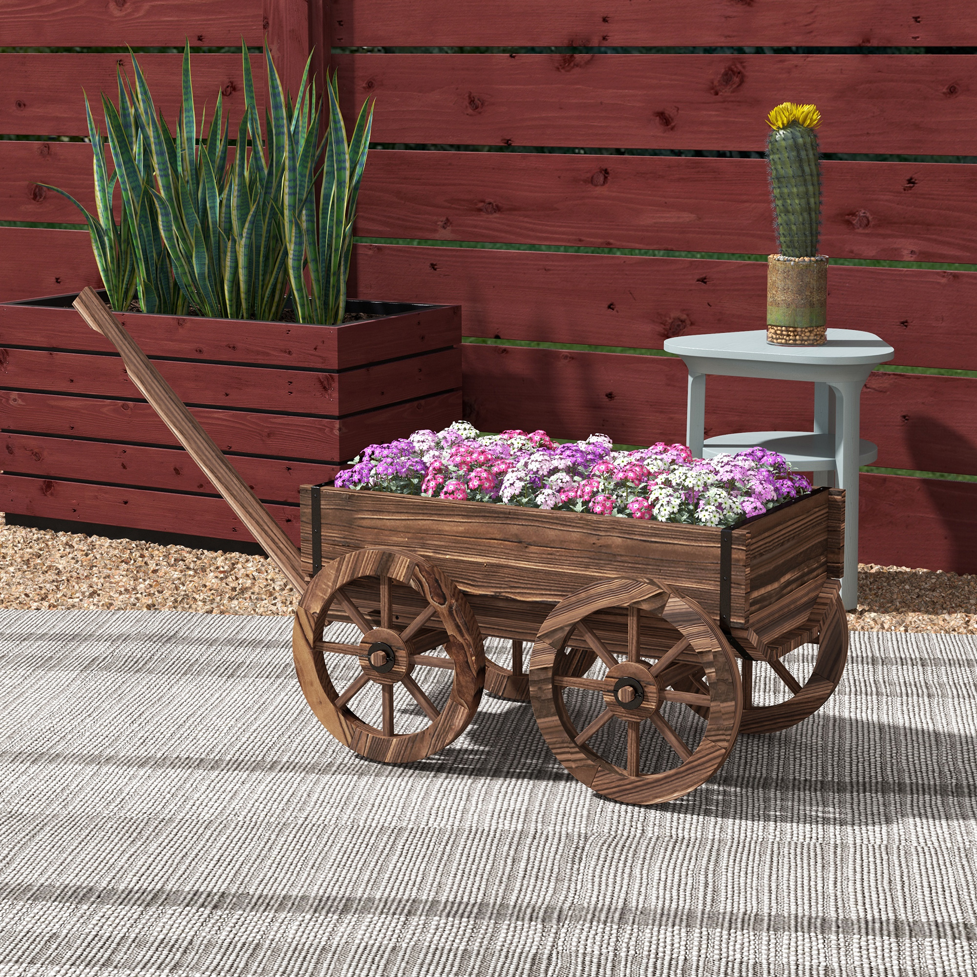 Holzwagen mit Blumen, Kaktus und Schlangenpflanzen vor Holzzaun.