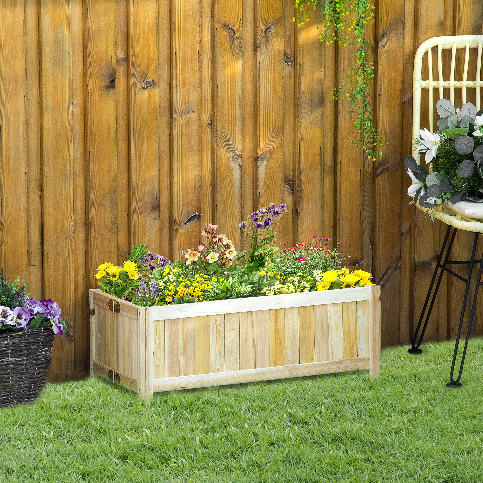 Ein hölzerner Blumenkasten mit bunten Blumen auf grünem Gras vor einem Holzzaun.