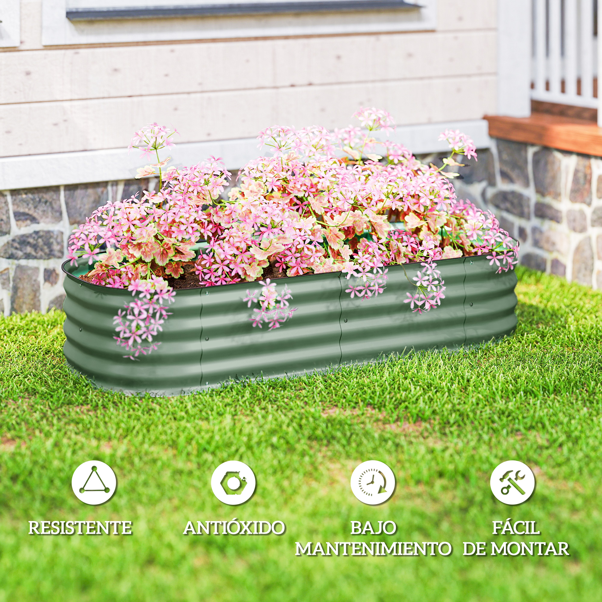 Un bancal verde elevado con flores rosas, junto a una casa.