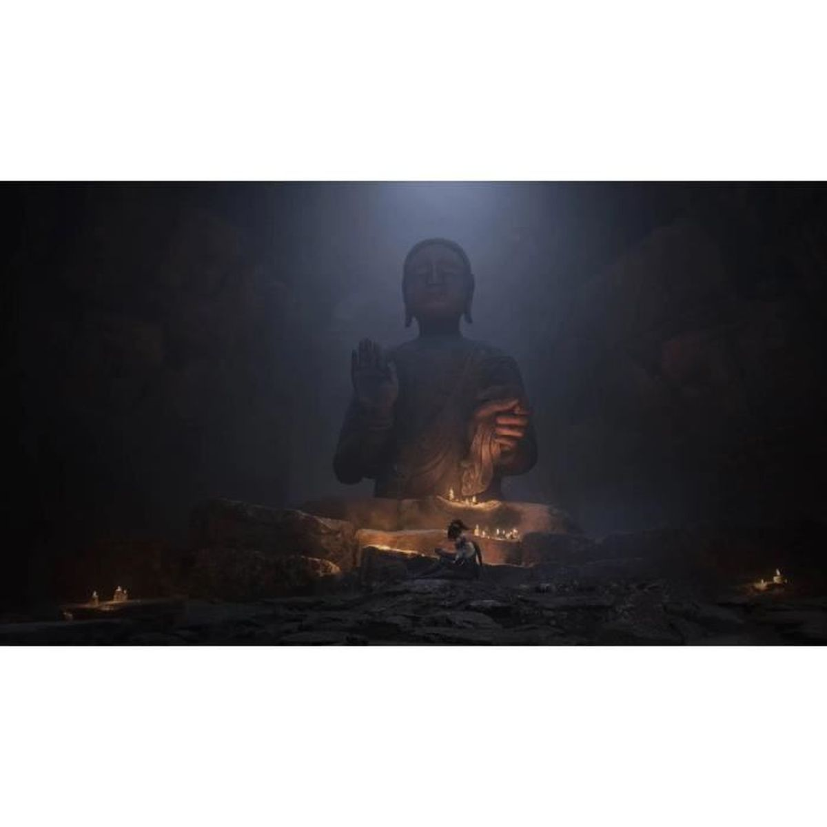 Una statua di Buddha nell'oscurità, illuminata da candele, con una piccola figura davanti.