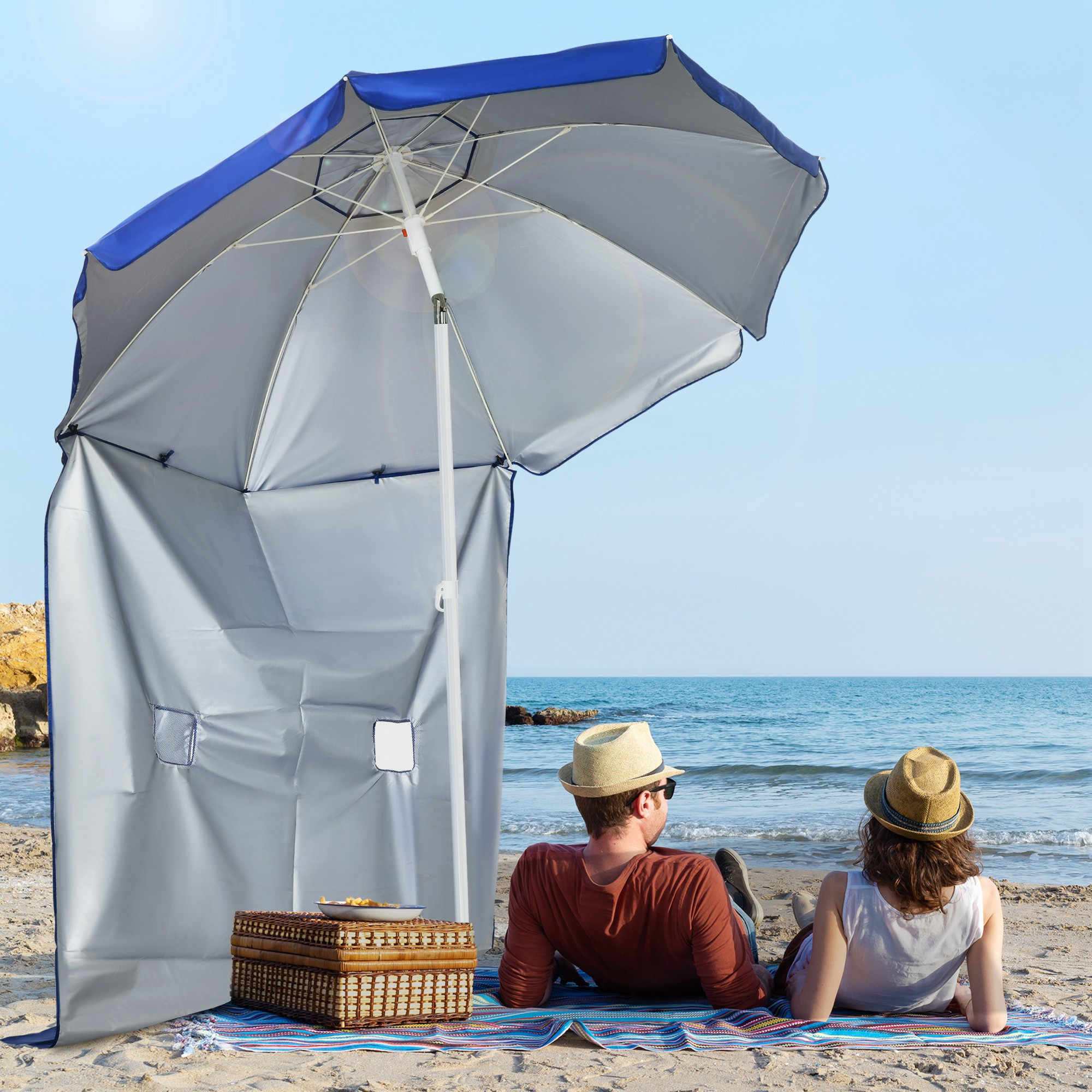Coppia in spiaggia sotto ombrellone con cesto da picnic.