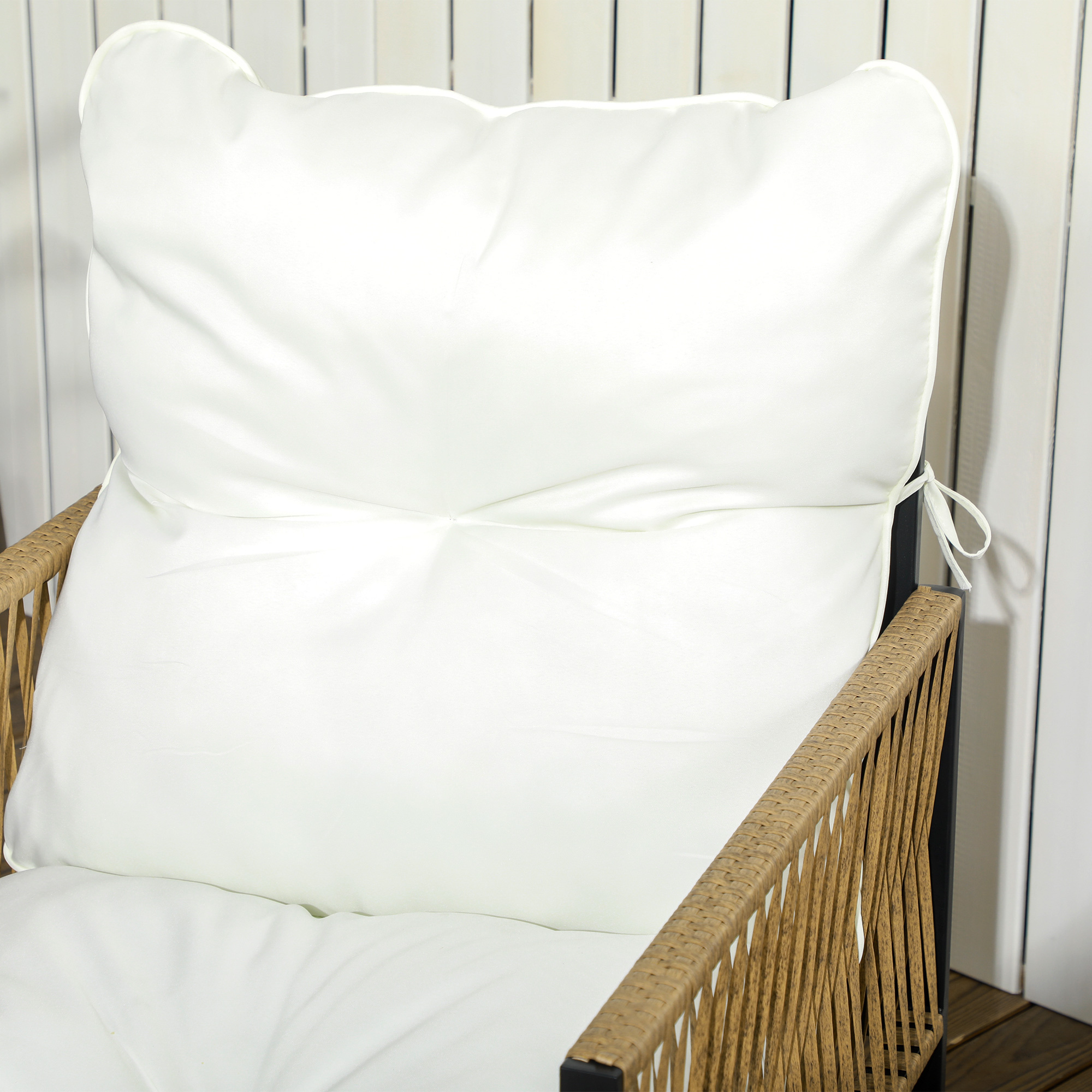 Un cojín blanco sobre una silla de ratán marrón contra un panel de madera blanco.