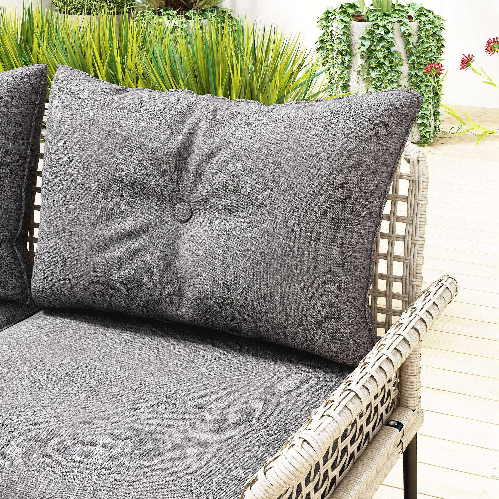 Cuscino grigio su divano da esterno in rattan con piante verdi.