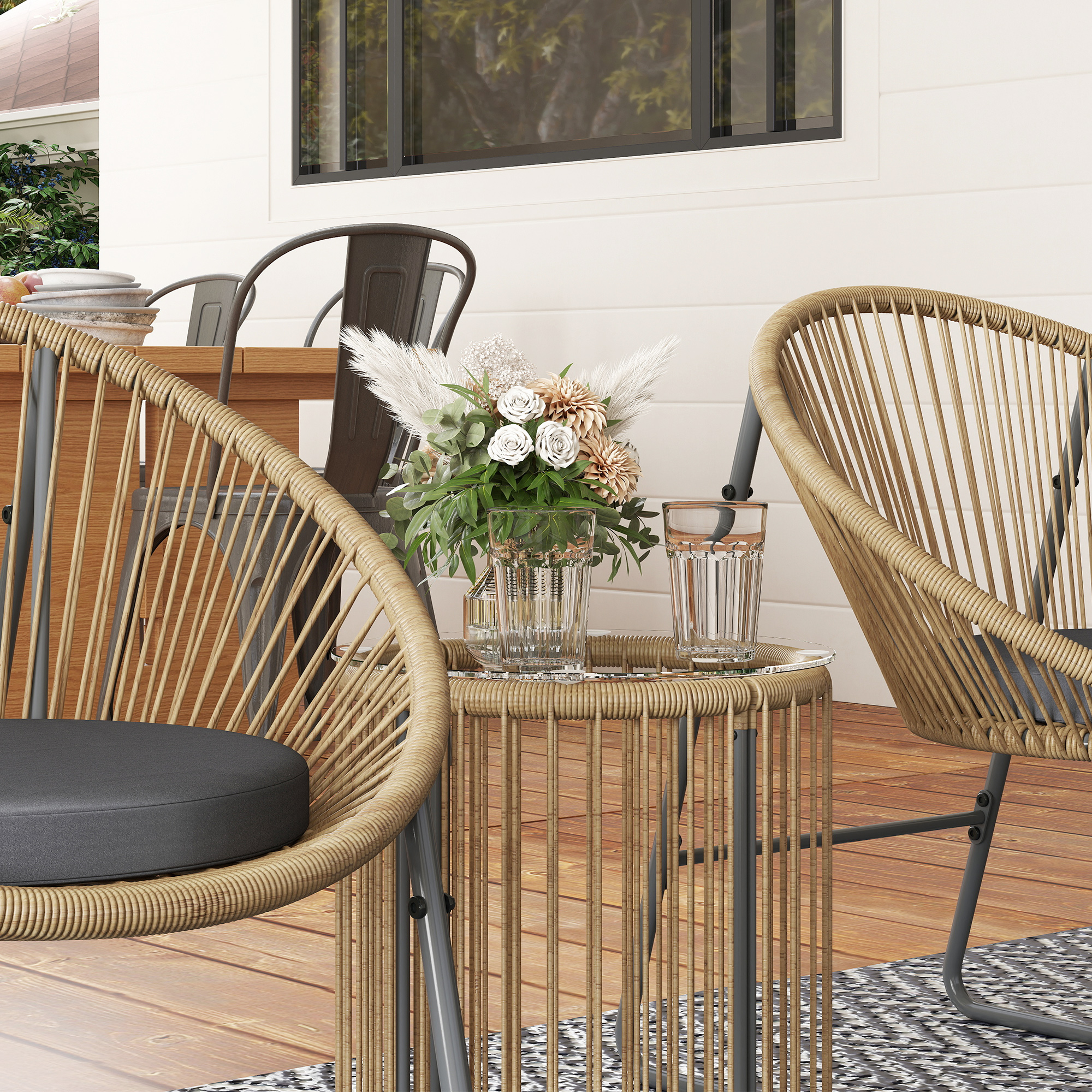 Due poltrone in rattan con cuscini grigi su un ponte di legno vicino a un tavolino con fiori e bicchieri.