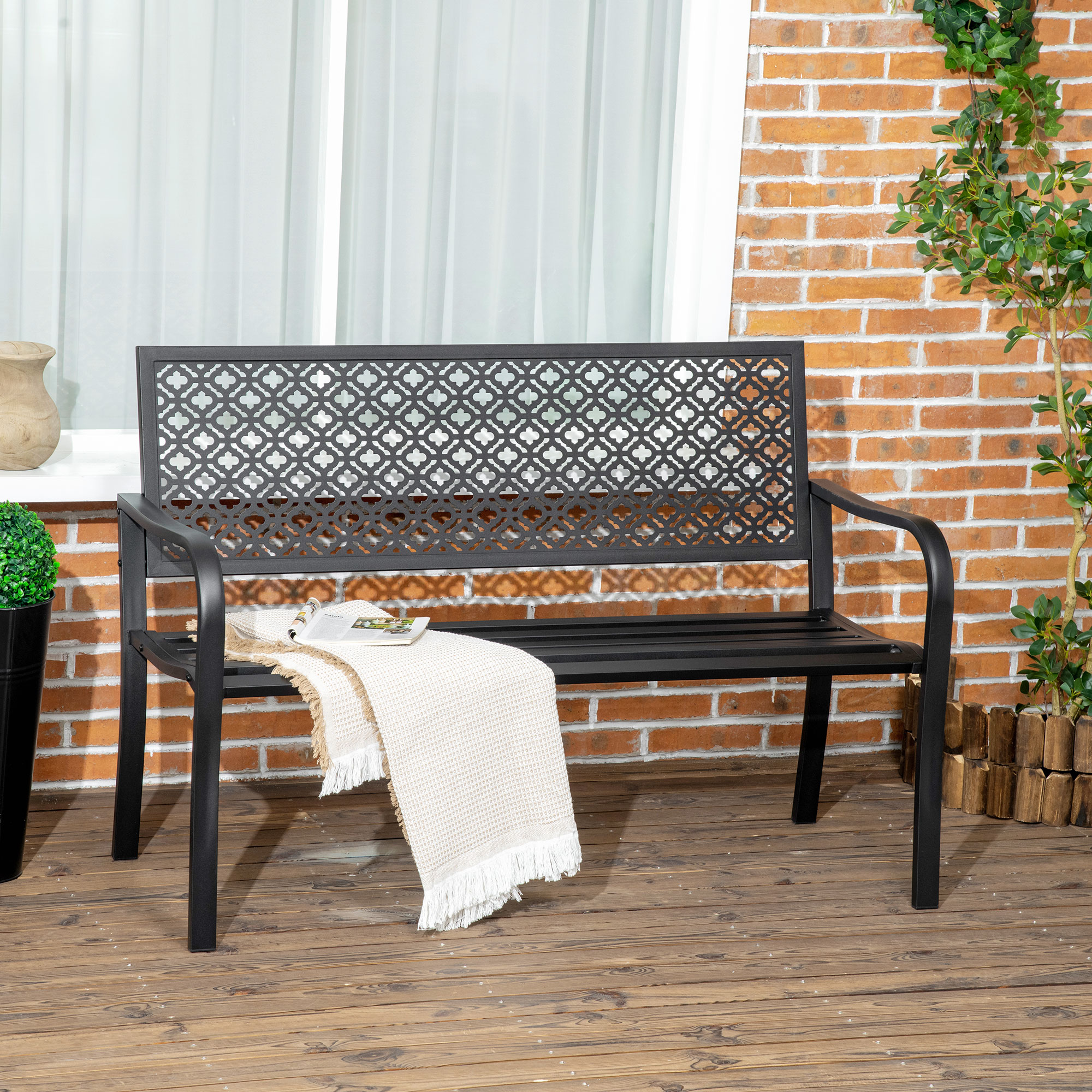 Banco de jardín de metal negro con respaldo estampado sobre tarima de madera.